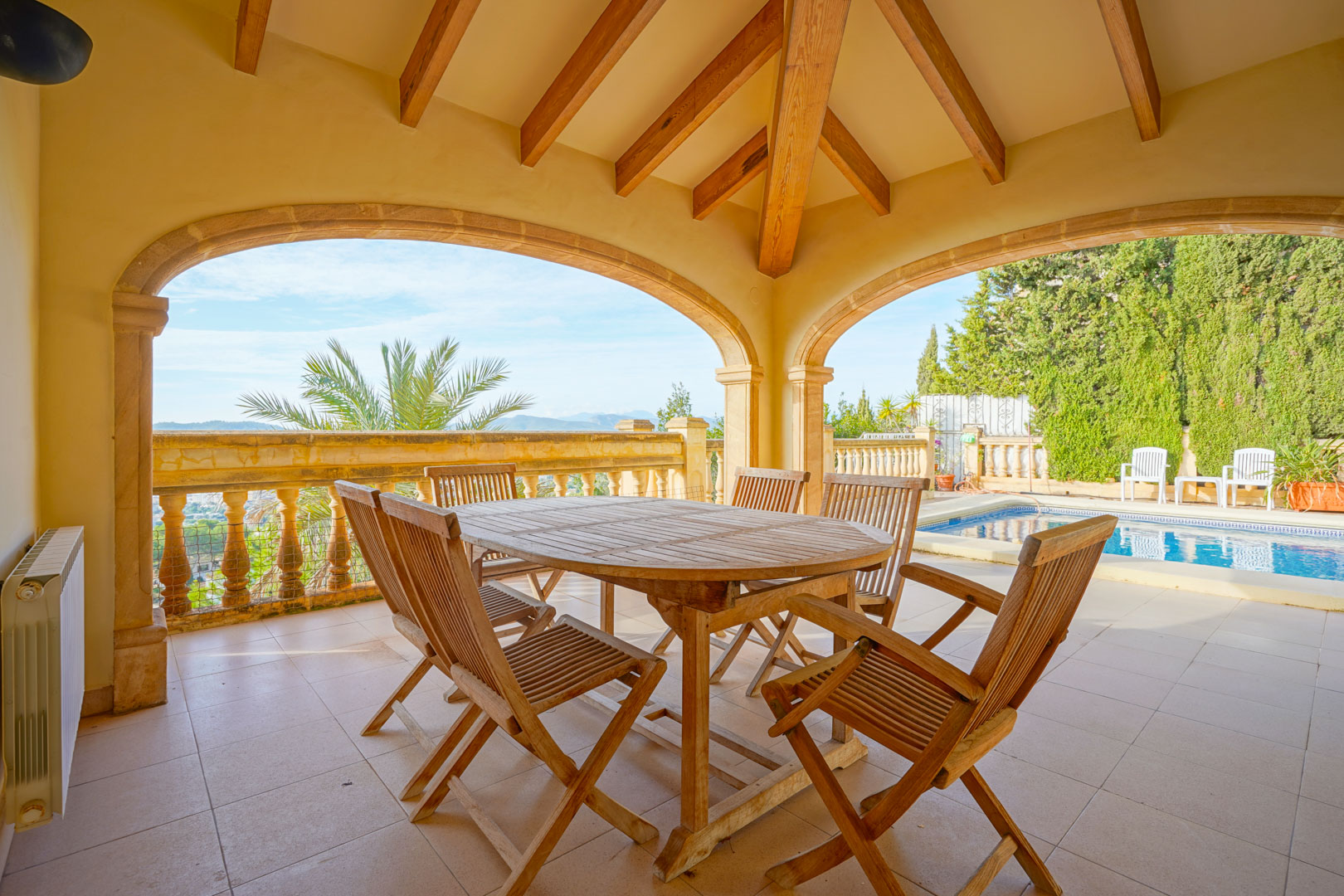 Überdachte Terrasse mit Holzbalkendecke und Steinbögen, ausgestattet mit Essbereich im Freien direkt am Pool mit Bergblick.