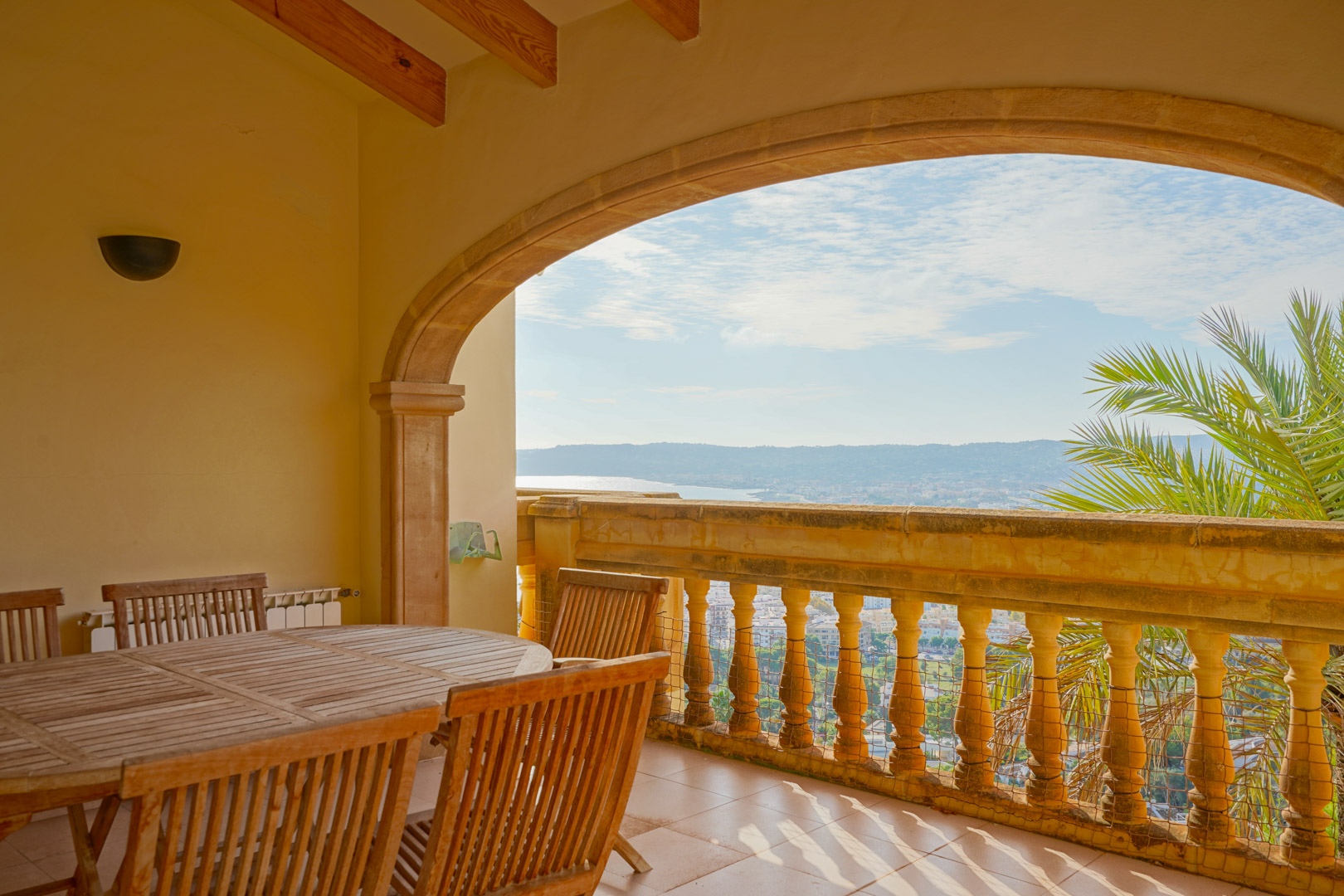 Überdachte Terrasse mit Natursteinbogen, Holzbalkendecke und Essbereich mit Panoramablick auf die Bucht von Jávea und die umliegende Berglandschaft.