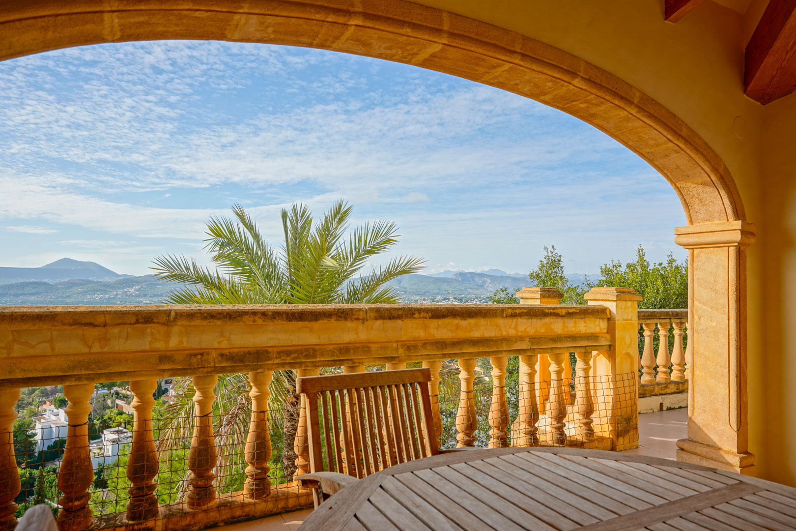 Überdachte Terrasse mit traditionellem Steinbogen und Balustrade, die einen Panoramablick auf die Berge und das Tal bietet, ausgestattet mit Holzmöbeln.