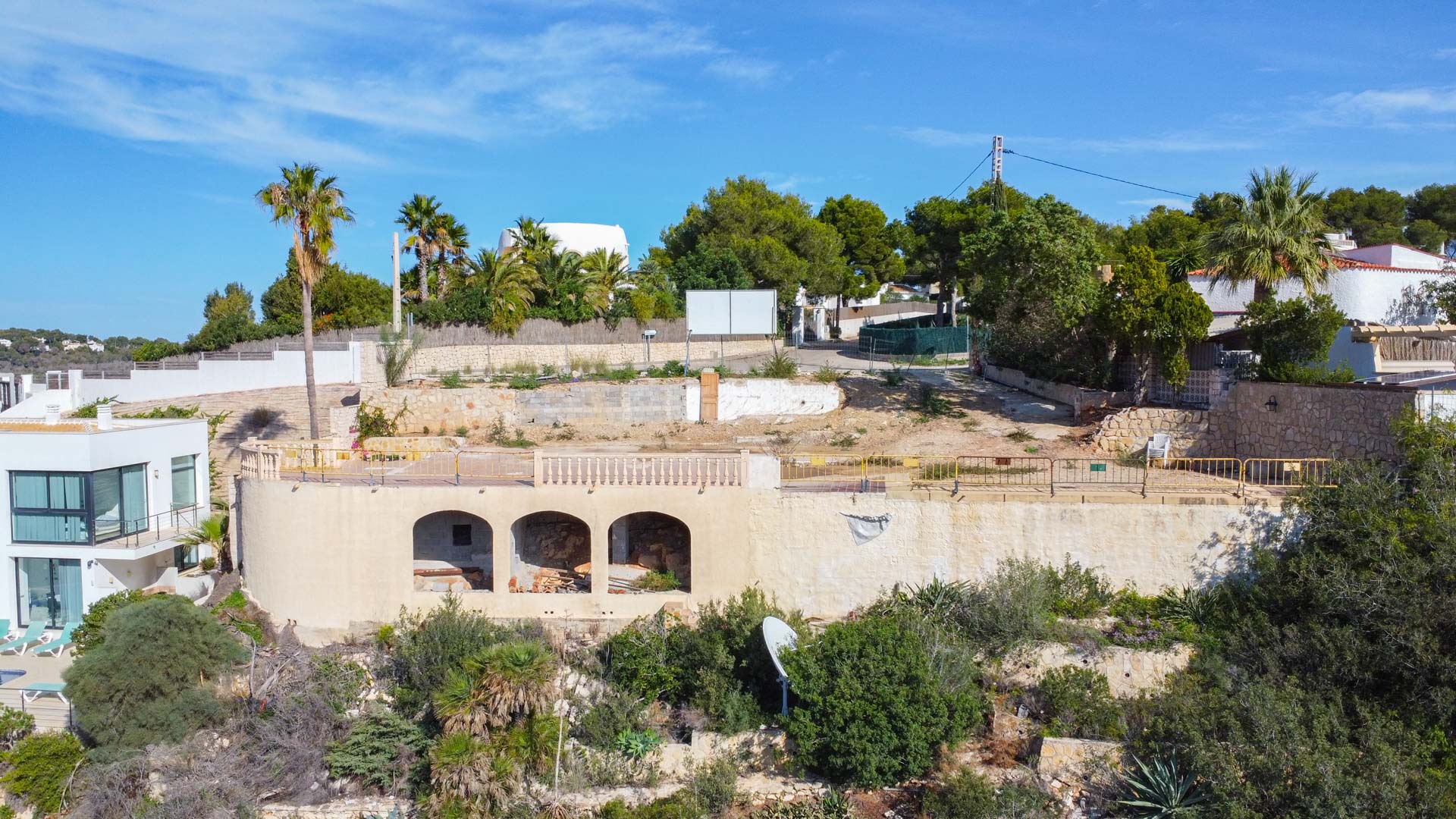Erhöhtes Baugrundstück mit bestehender Bogenstruktur, Natursteinmauern und mediterraner Bepflanzung, vorbereitet für den Bau einer Luxusvilla.