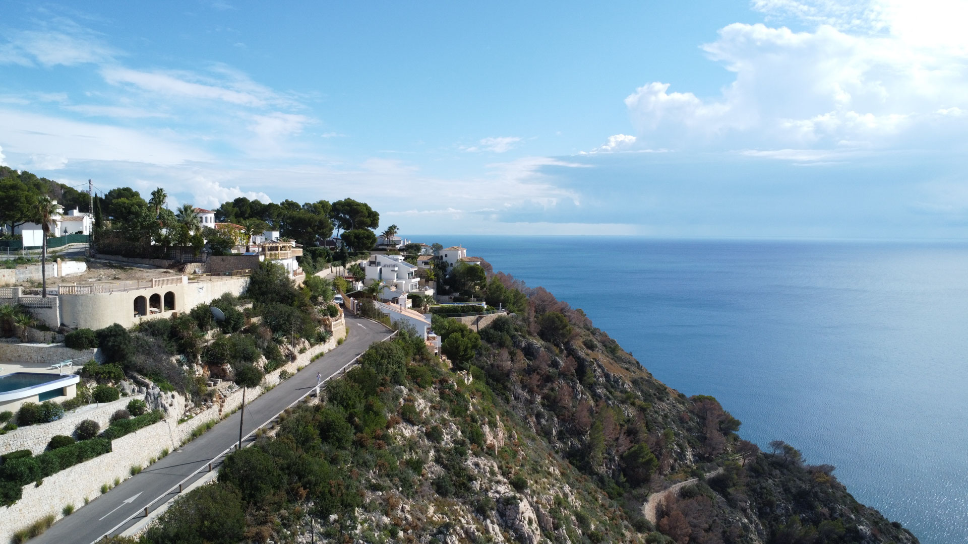 Luftaufnahme der Küste von Granadella in Jávea mit Grundstücken in Hanglage, direktem Blick auf das Mittelmeer und asphaltierter Zufahrtsstraße.