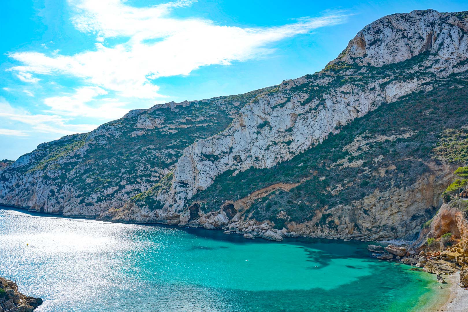 Panoramablick auf das türkisfarbene Wasser der Bucht von Granadella, umrahmt von schroffen Kalksteinfelsen und mediterraner Vegetation.