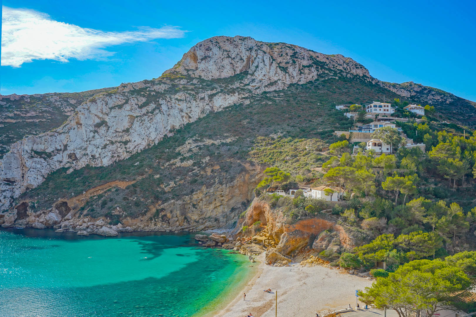 Panoramablick auf die Bucht von Granadella mit türkisfarbenem Wasser, Kalksteinfelsen und mediterraner Vegetation an der Kieselstrandküste.