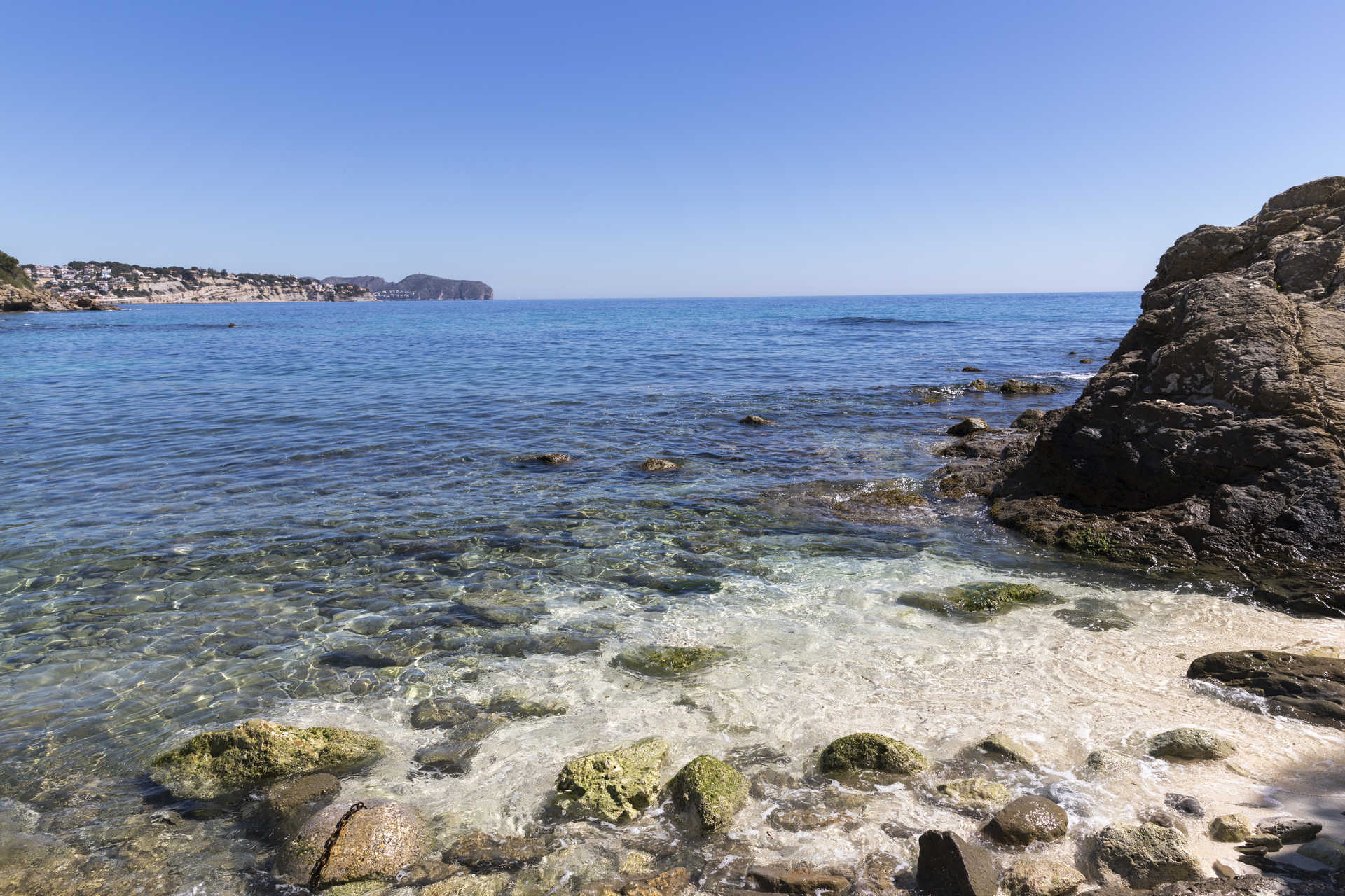 Blick auf die Mittelmeerküste mit kristallklarem Wasser und felsigem Ufer in der Nähe des Strandes La Fustera, der die unmittelbare Nähe zum Meer zeigt.