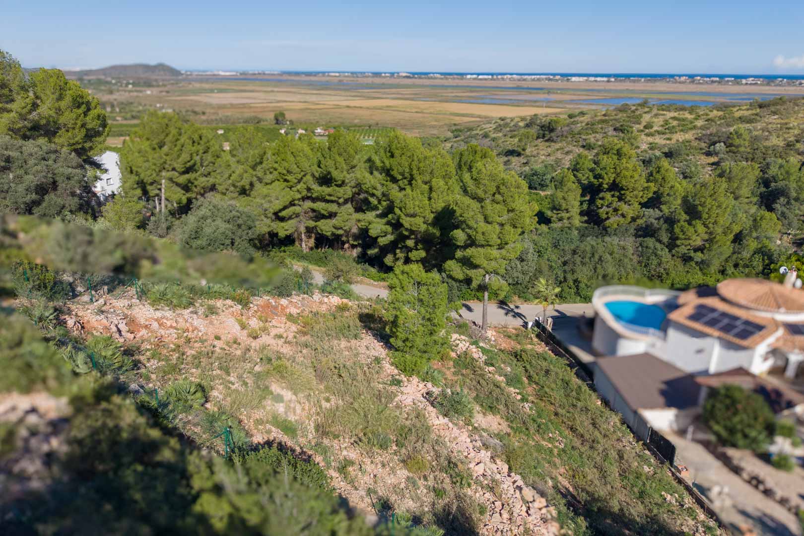 Erhöhtes Grundstück mit Umzäunung und weitem Blick auf den Naturpark Marjal de Pego sowie das ferne Mittelmeer.
