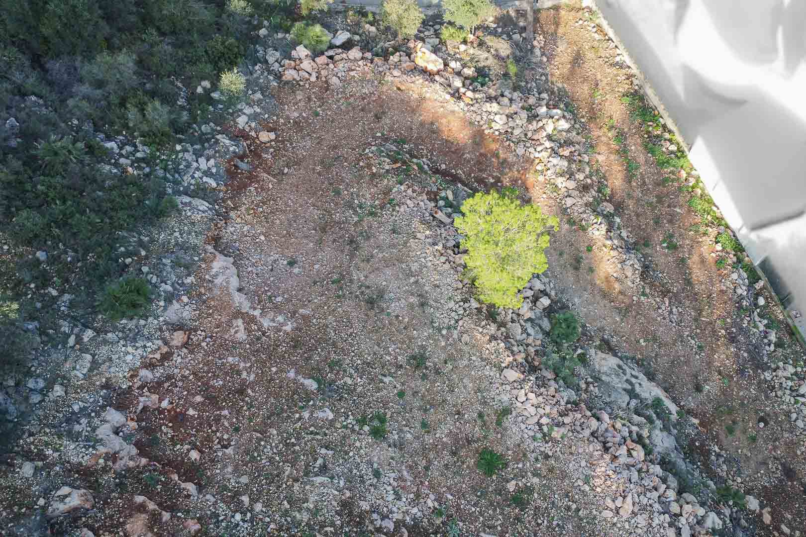 Luftaufnahme des Baugrundstücks mit felsigem Untergrund und mediterraner Bepflanzung. Das Gelände ist für die Bebauung vorbereitet und verfügt über eine klare Begrenzung.