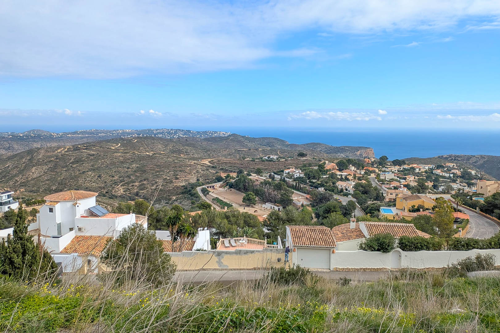 Erhöhter Panoramablick von Cumbre del Sol auf das Mittelmeer, der die küstennahe Wohnlandschaft und die umliegenden Hügel der Costa Blanca zeigt.