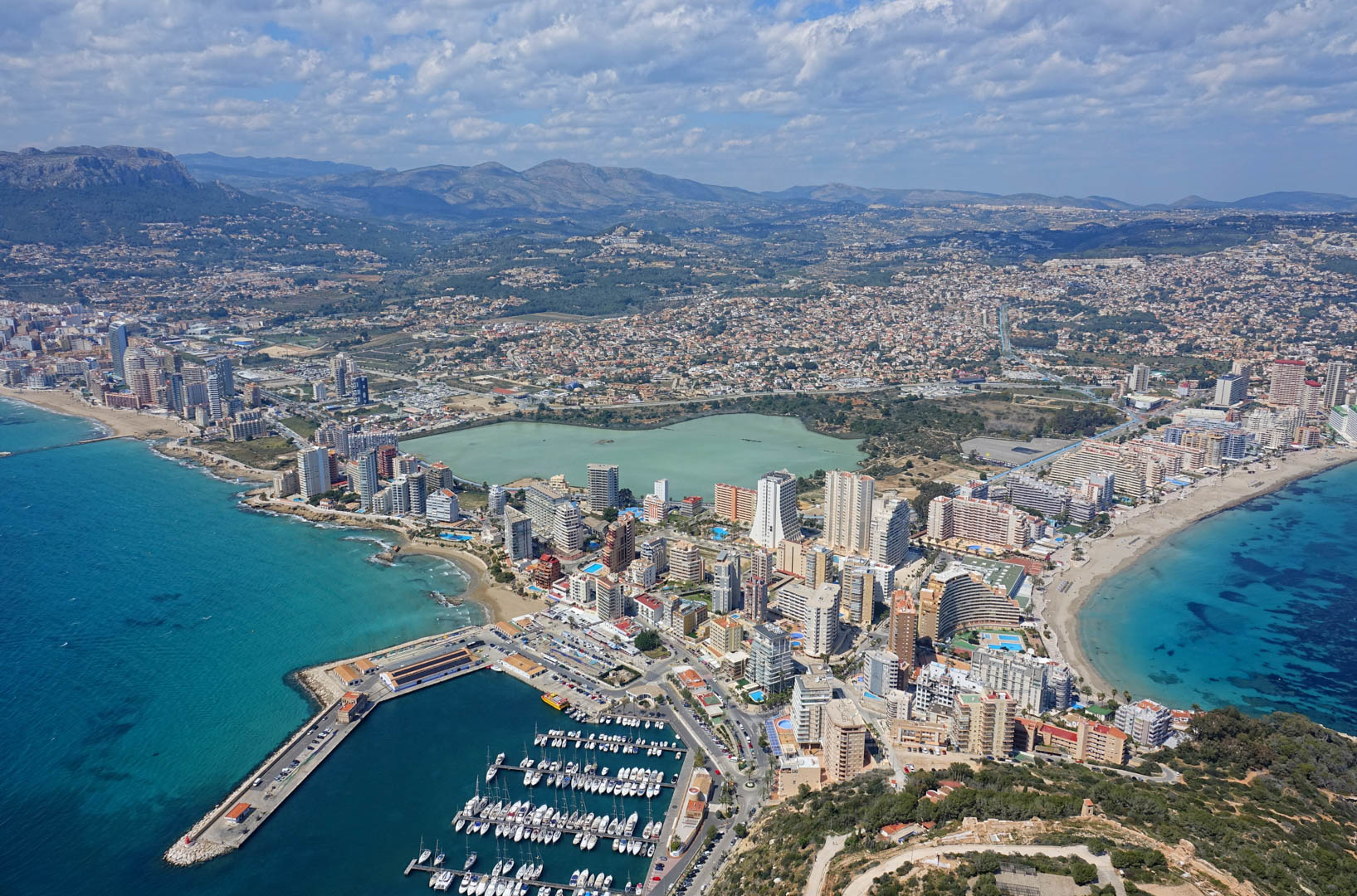 Panorama-Luftaufnahme von Calpe mit dem Jachthafen, Sandstränden, dem Salzsee Las Salinas und der Skyline vor der Kulisse der fernen Berge.