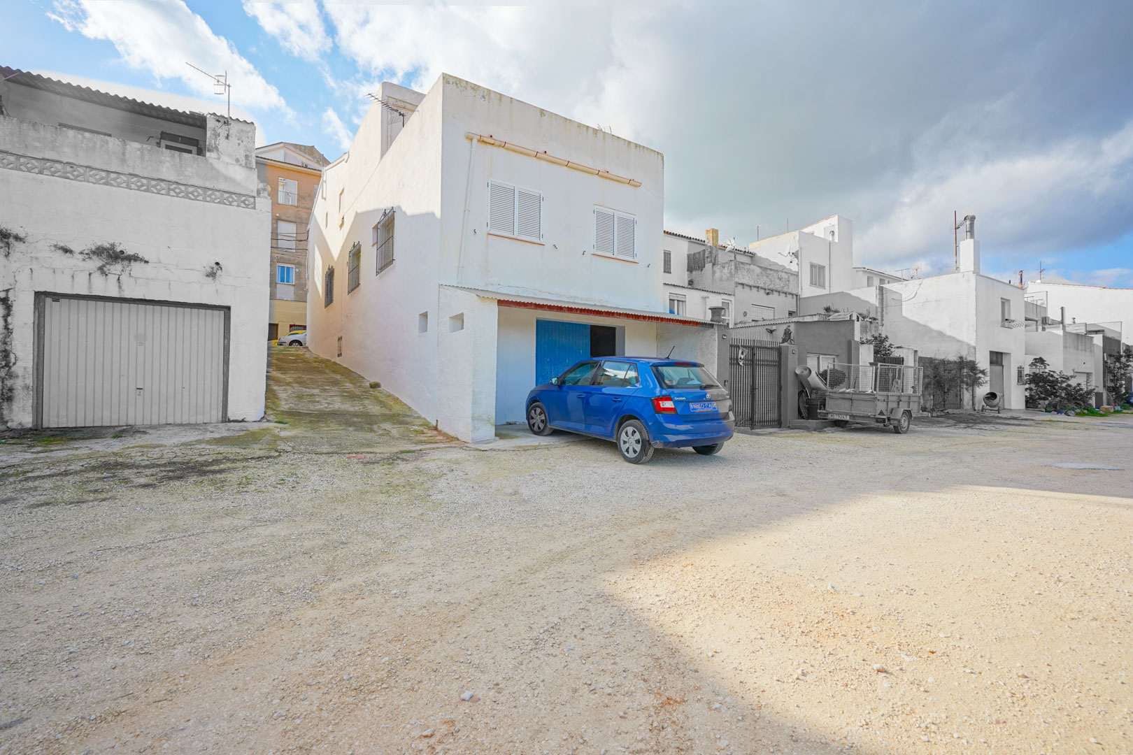 Außenfassade der Immobilie in Benissa mit Zugang zur Souterrain-Garage, einer seitlichen Rampe und Fenstern mit weißen Fensterläden.
