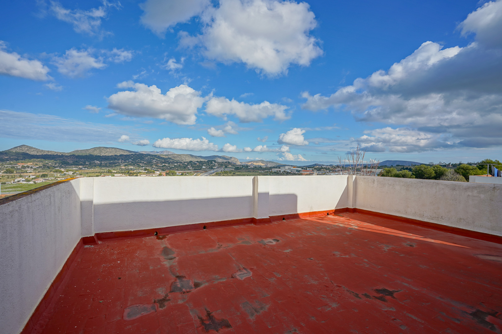 Dachterrasse mit rotem Bodenbelag und weißen Umfassungsmauern, die einen weiten Panoramablick auf die umliegende Berglandschaft bietet.