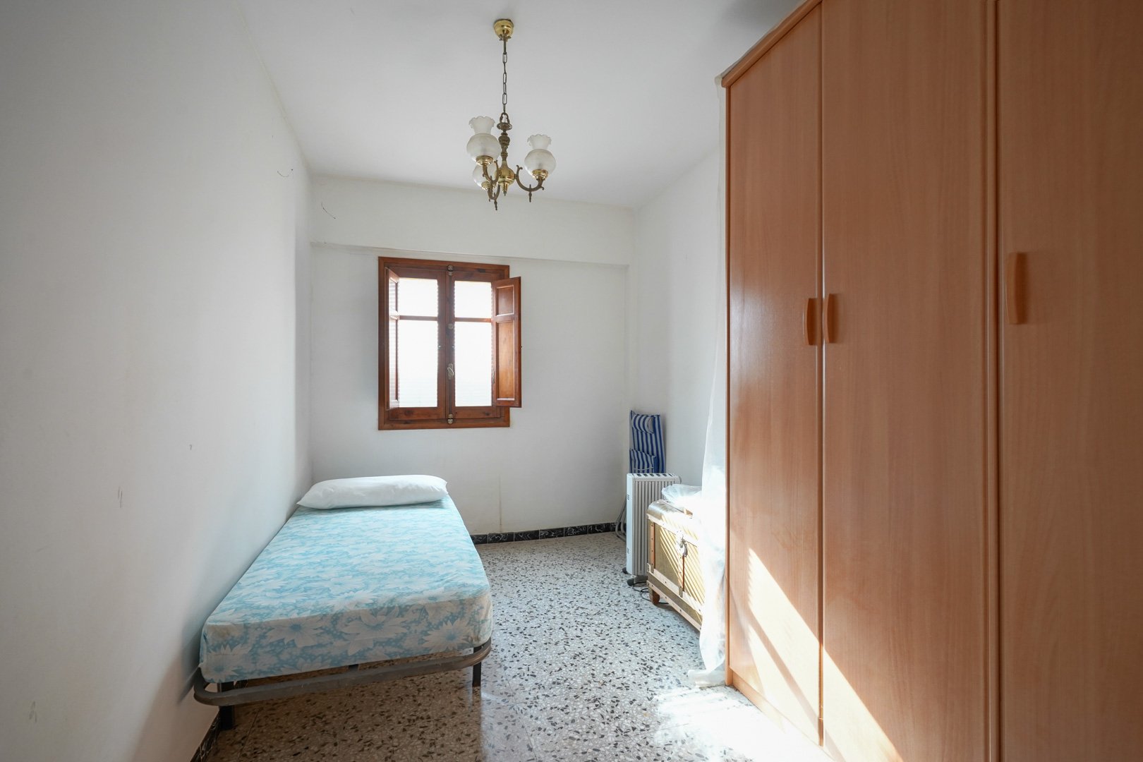 Einzelzimmer mit traditionellem Terrazzoboden, einem großen Holzschrank und einem Holzfenster mit Innenläden für natürliches Licht.