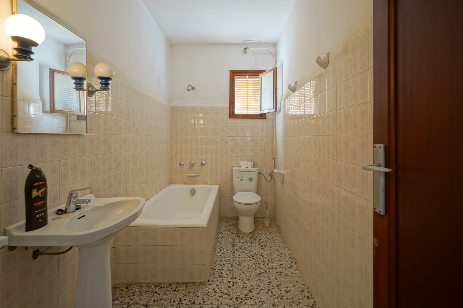 Funktionales Badezimmer mit Einbaubadewanne, Standwaschbecken, Terrazzoboden und klassisch gemusterten Wandfliesen.