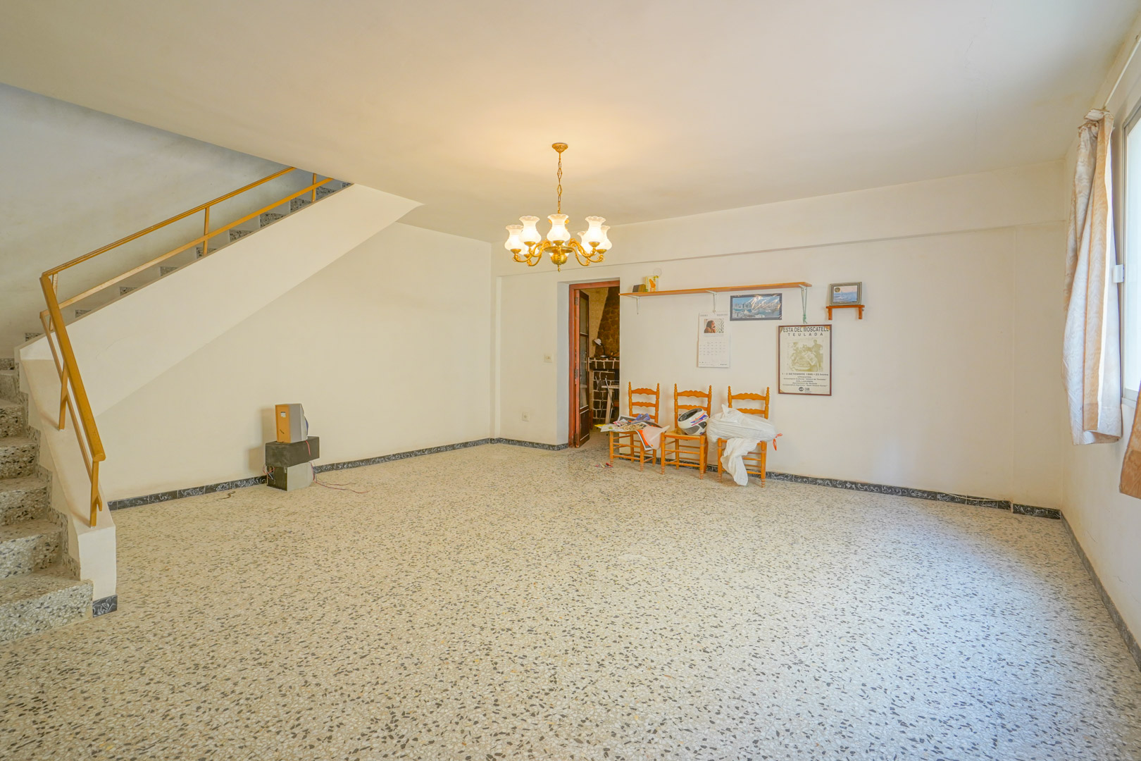 Hauptwohnbereich mit originalem Terrazzoboden, klassischem Kronleuchter und Treppe mit Metallgeländer, die in das Obergeschoss führt.