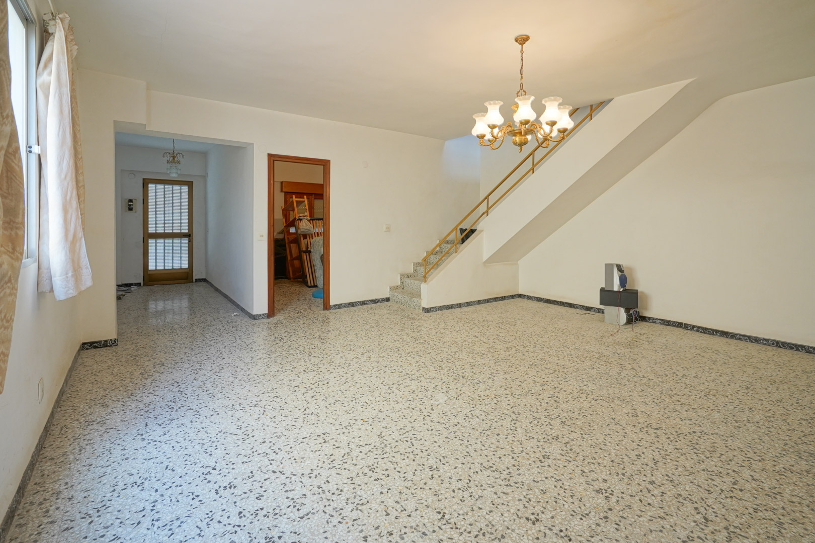 Hauptwohnzimmer mit originalem Terrazzoboden, integrierter Treppe mit Metallgeländer und Zugang zum Flur und den Schlafzimmern.