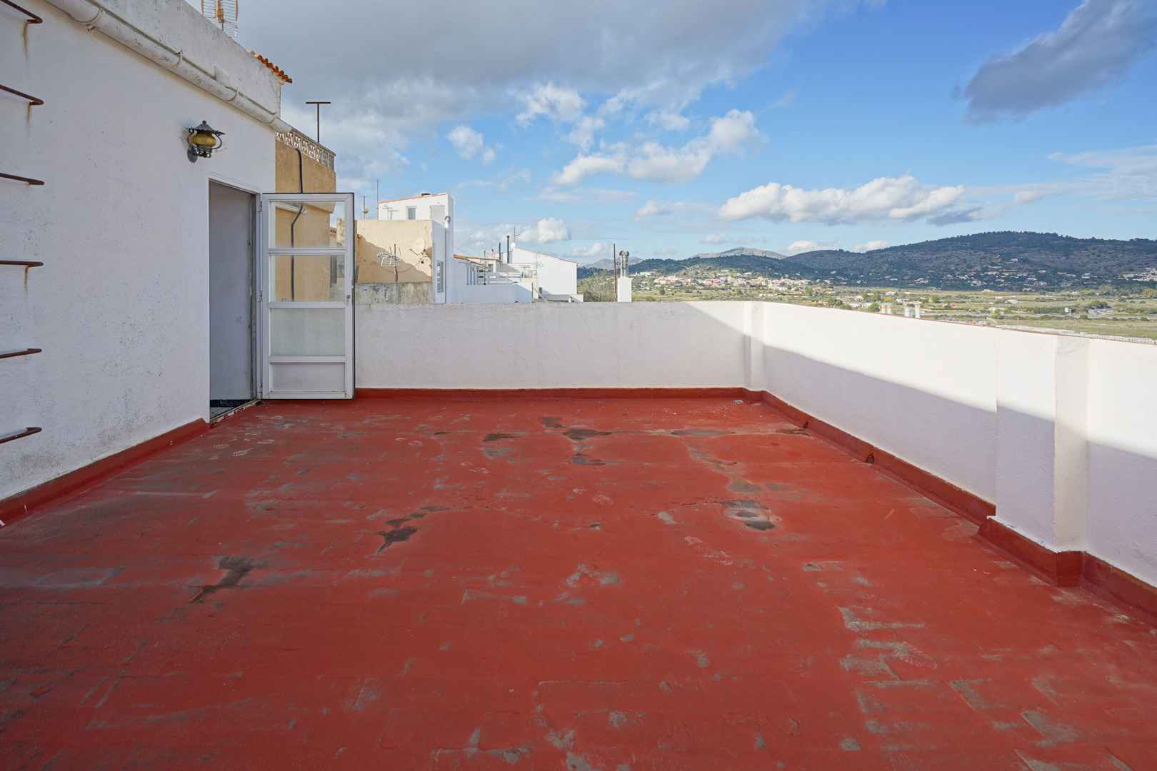 Obere Terrasse mit rotem Fliesenboden und weißen Mauern, die einen weiten Panoramablick auf die umliegenden Berge und die Landschaft bietet.