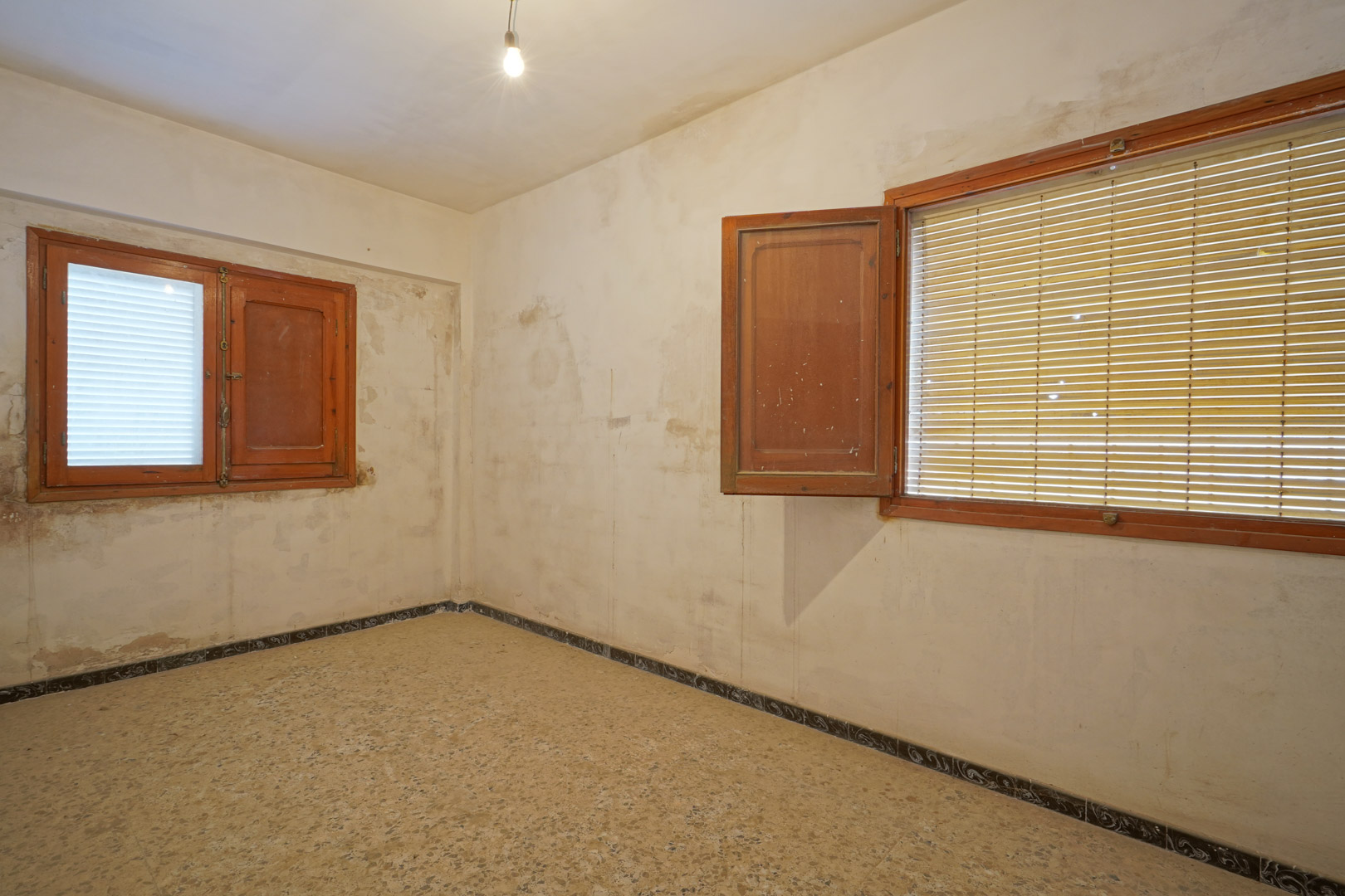 Renovierungsbedürftiges Schlafzimmer mit originalem Terrazzoboden, Holzfenstern mit Fensterläden und Wänden, die Raum für Gestaltung bieten.
