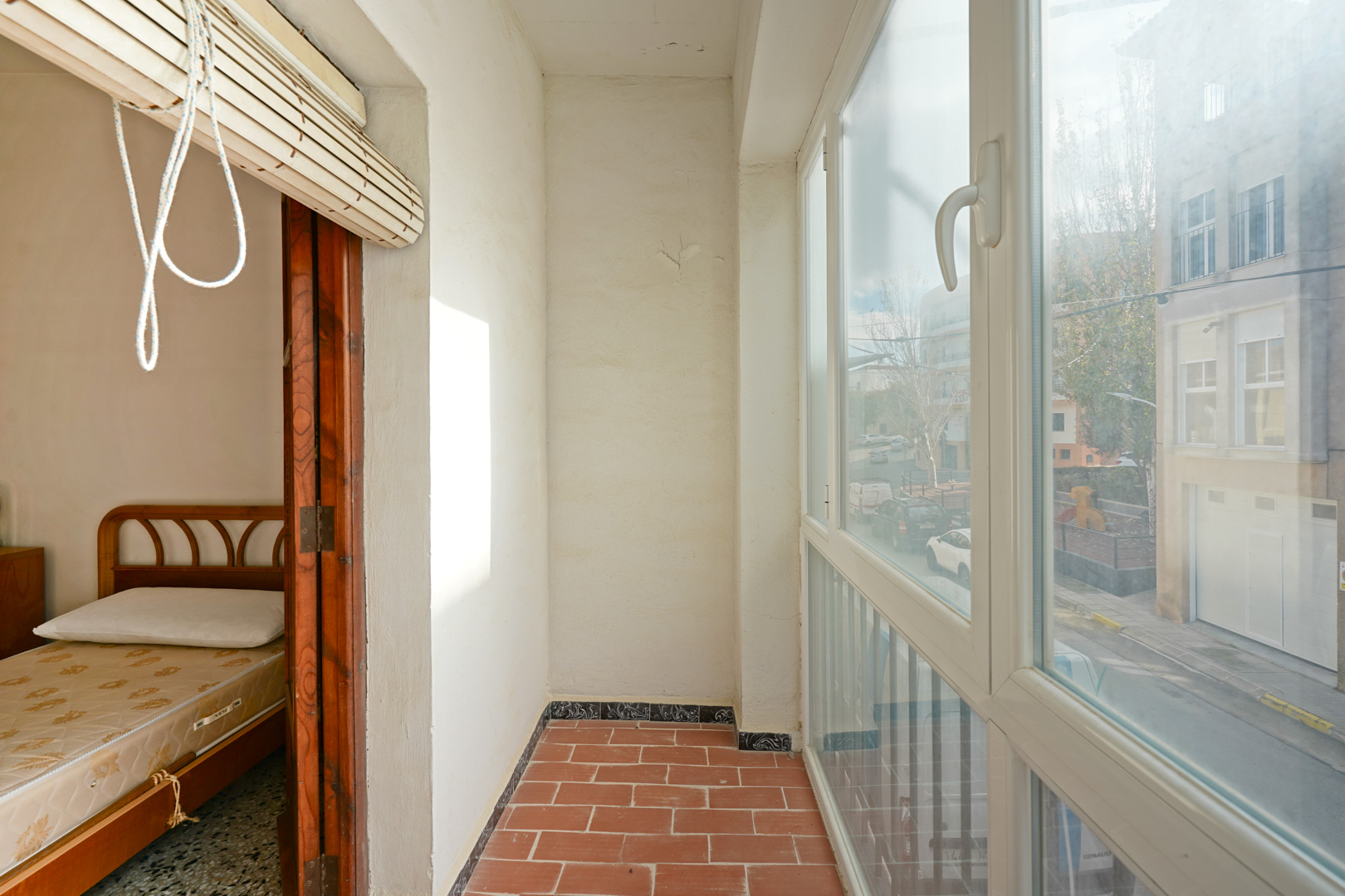 Verglaste Terrasse mit rustikalen Terrakotta-Fliesen, weißen PVC-Fenstern und Blick auf die Straße sowie direktem Zugang zu einem der Schlafzimmer.
