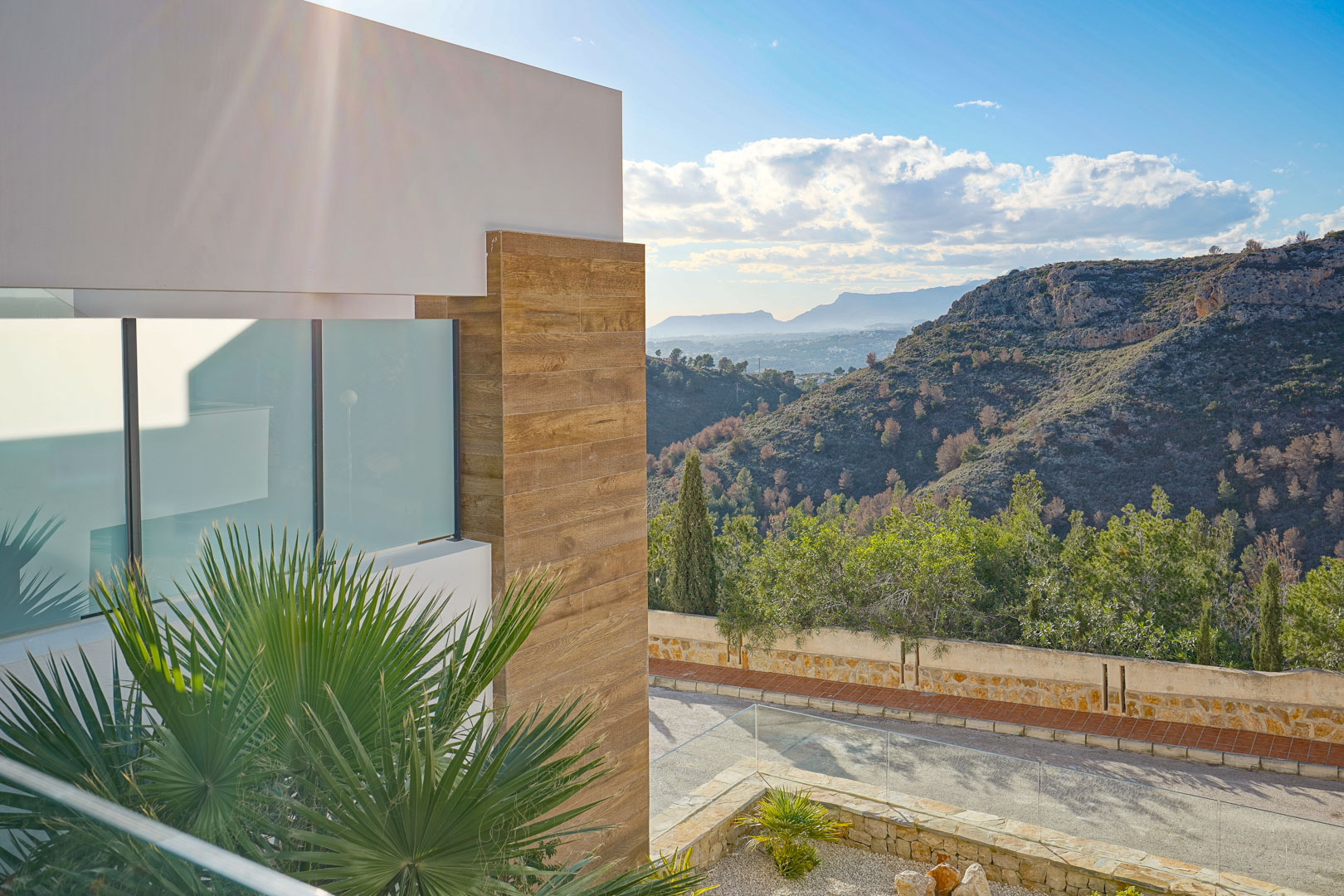 Außenansicht von der Terrasse mit Glasgeländer, moderner Holzoptik-Fassade und weitem Blick über den angrenzenden Naturpark und die Berge.