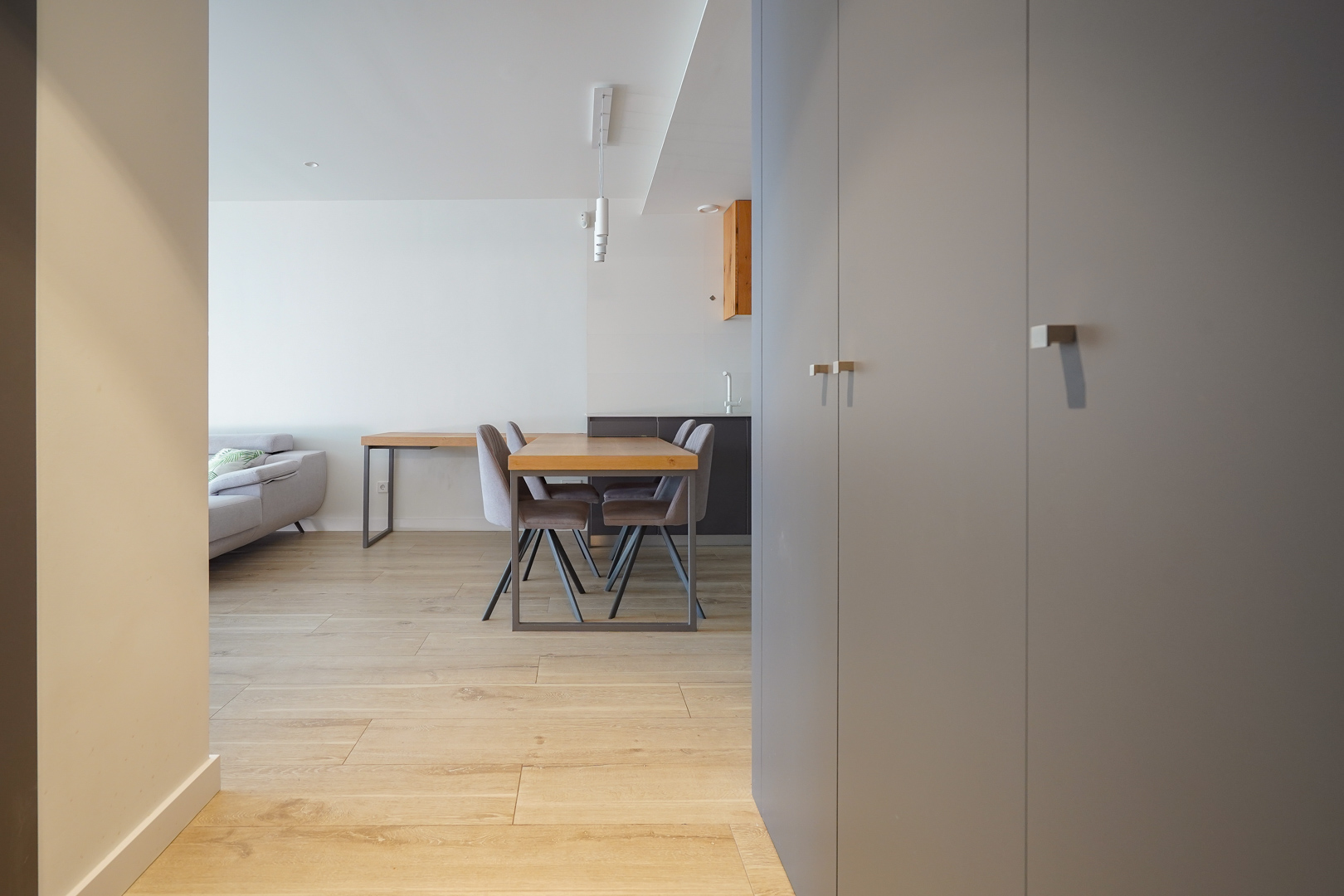 Eingangsbereich mit grauen Einbauschränken, hellem Holzboden und offenem Essbereich mit Holztisch und moderner Beleuchtung.