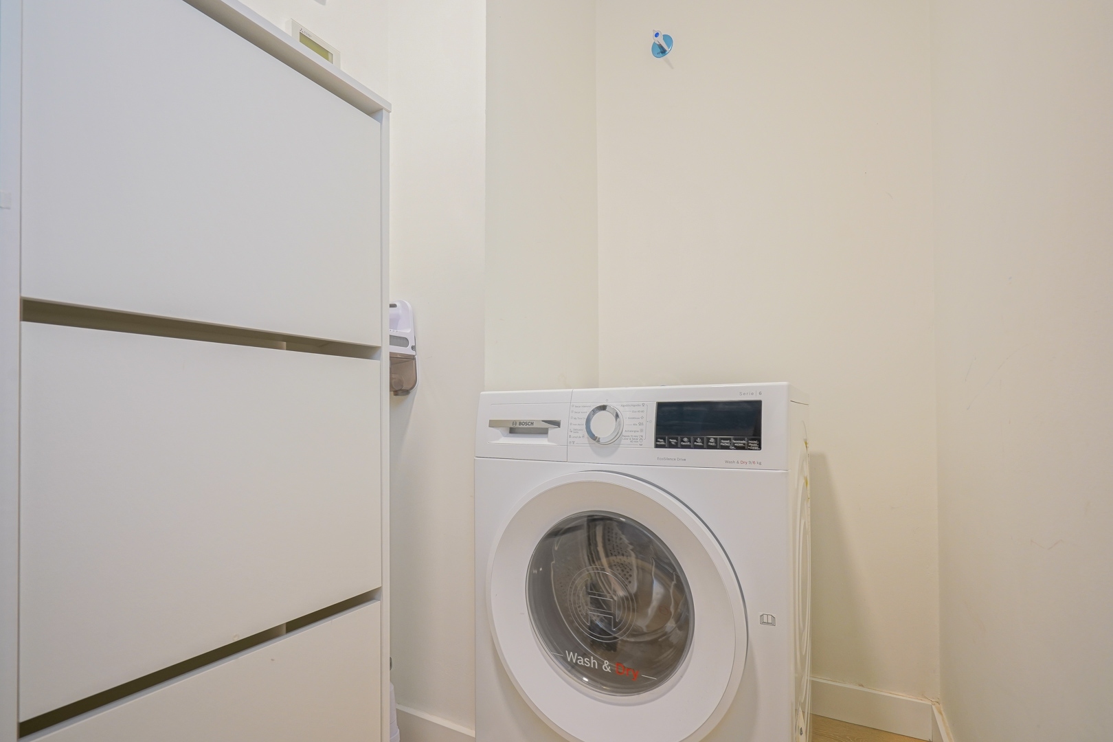 Funktionaler Hauswirtschaftsraum mit Bosch Waschtrockner und weißem Vorratsschrank, direkt neben dem Eingangsbereich gelegen.