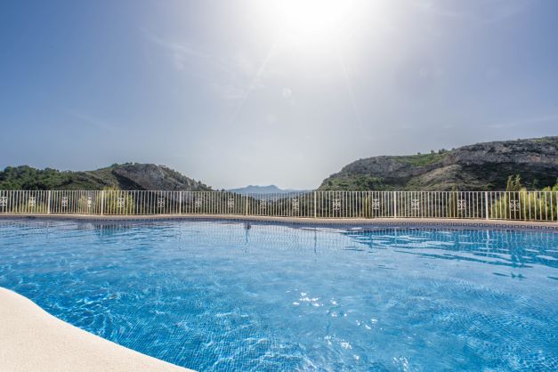 Gemeinschaftspool in Monte Cala Gardens mit freiem Blick auf die Berge und den Naturpark unter strahlendem Sonnenschein.