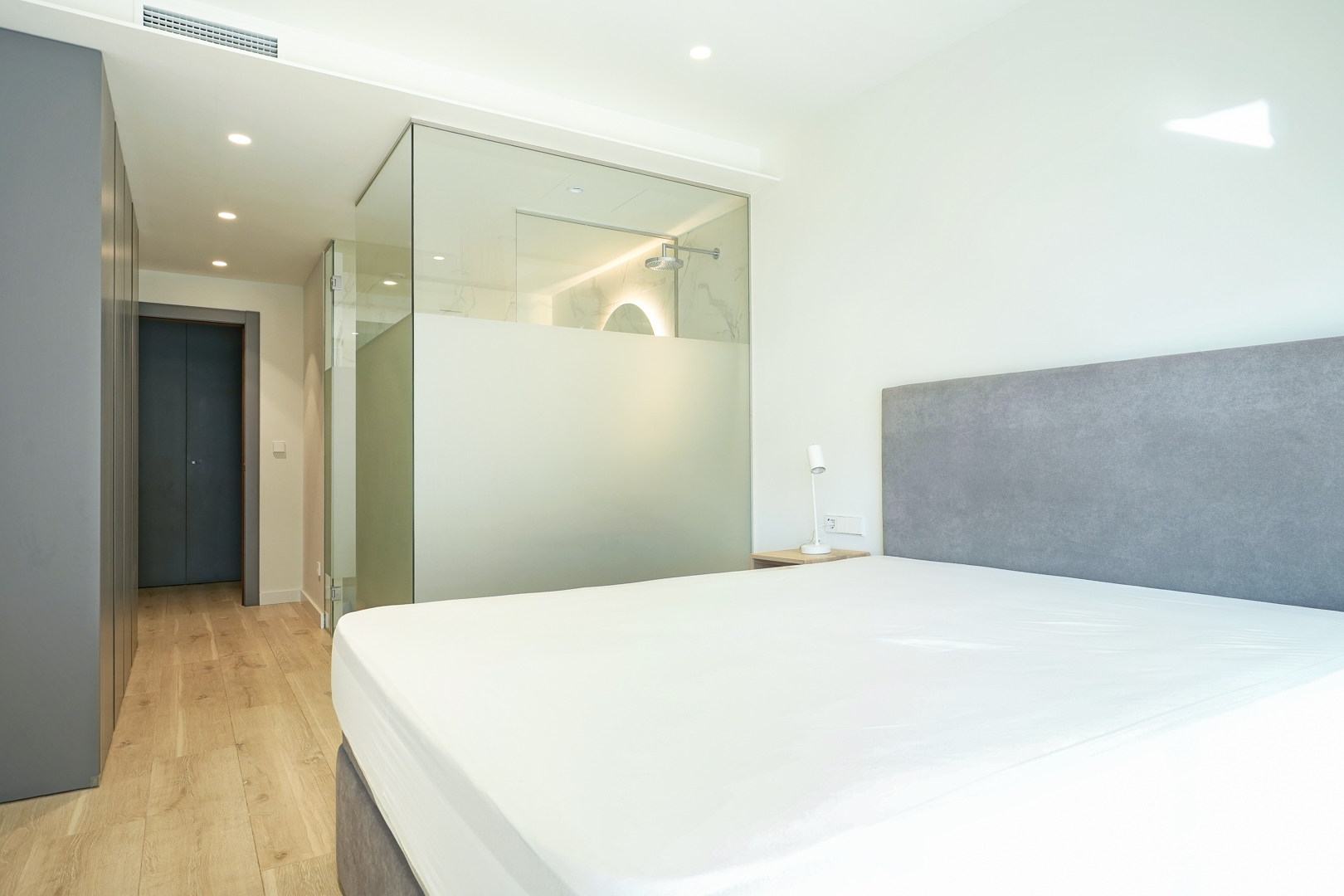 Hauptschlafzimmer mit integriertem En-Suite-Badezimmer durch Glastrennwände, Einbauschränken und hellem Holzboden.