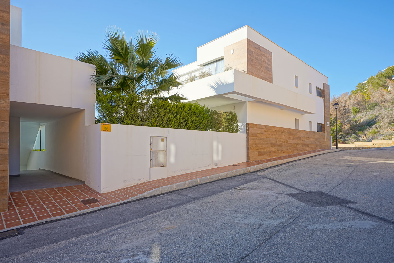 Moderne Außenansicht der Anlage Monte Cala Gardens mit weißer Fassade, Akzenten in Holzoptik und einem überdachten Zugangsweg.
