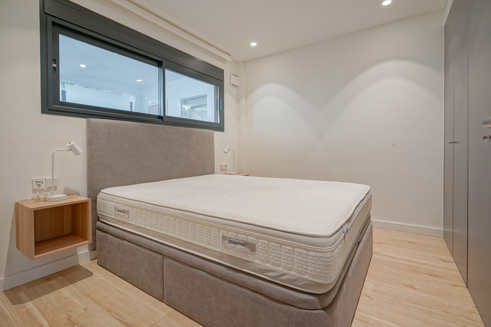 Modernes Schlafzimmer mit Doppelbett, gepolstertem Kopfteil, Einbauschränken und hellem Holzboden unter Decken-Einbaustrahlern.
