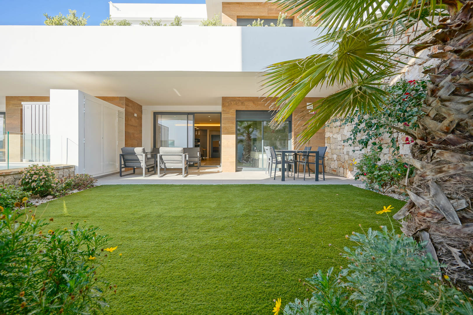 Überdachte 23 m2 Terrasse mit Sitzbereich und ein 36 m2 privater Garten mit Kunstrasen, begrenzt durch eine Natursteinmauer und direktem Zugang zur Wohnung.