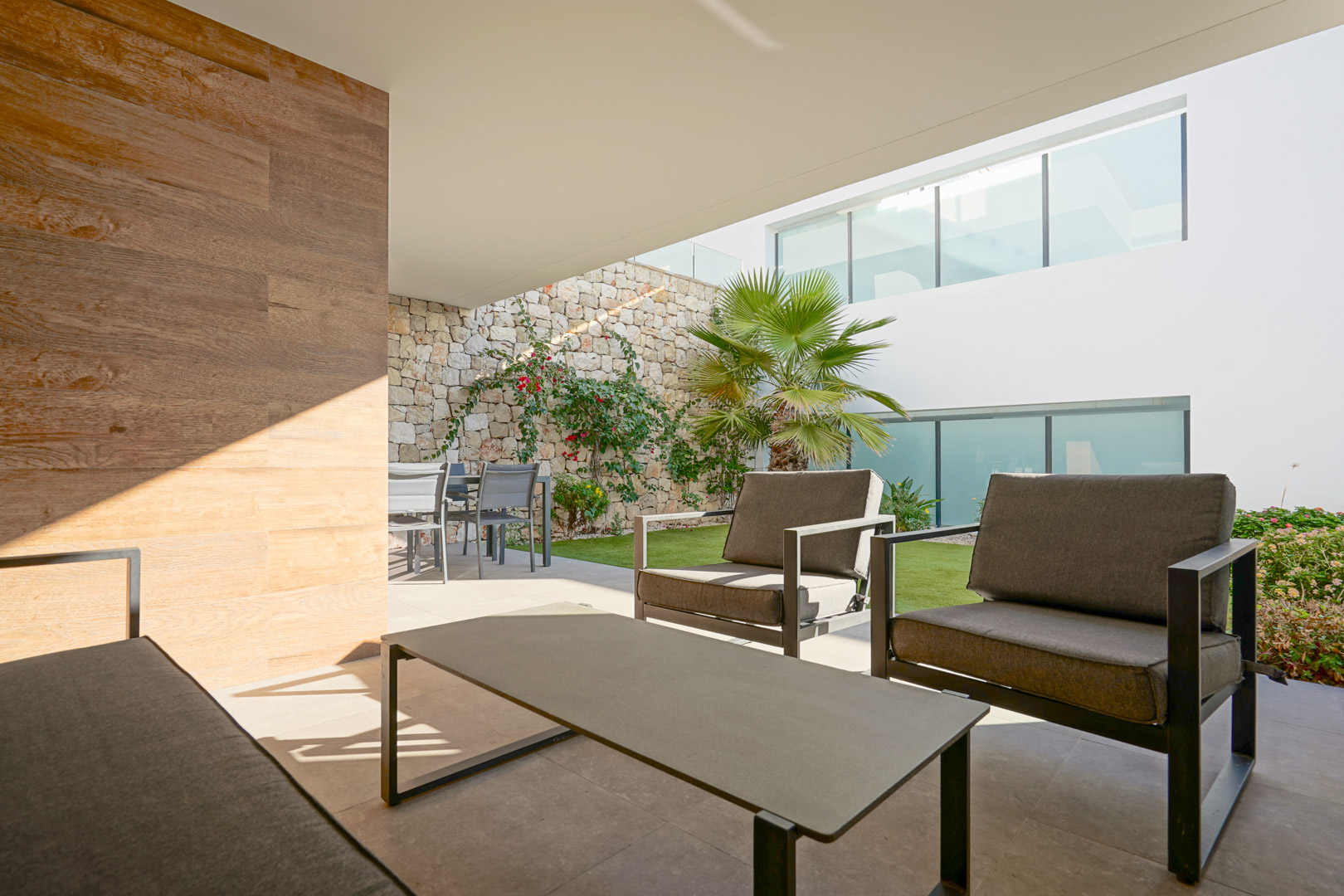Überdachte Terrasse mit modernem Loungebereich, Essplatz und privatem Garten, eingefasst von einer Natursteinmauer.