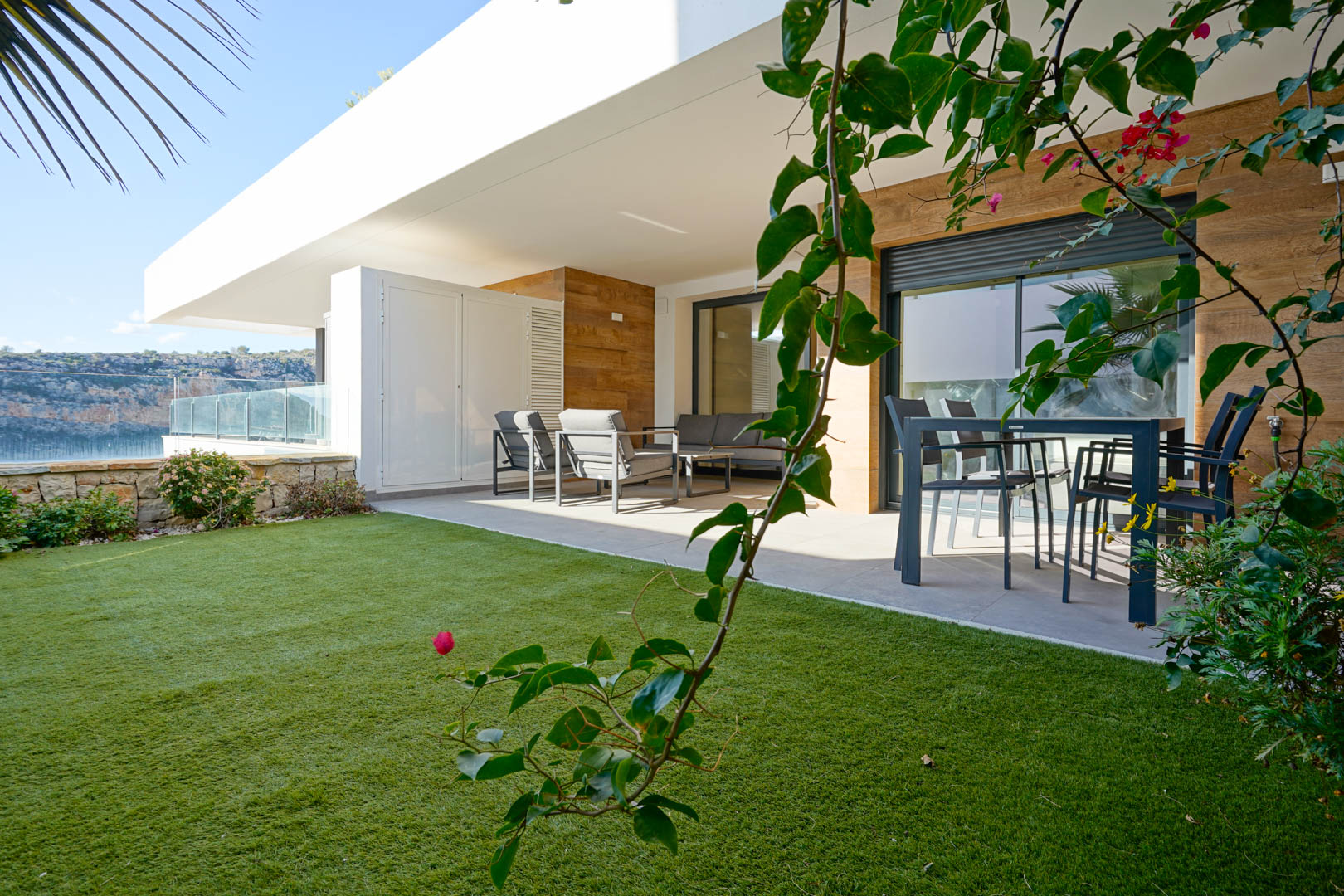 Überdachte Terrasse mit modernen Gartenmöbeln und privatem Rasen, begrenzt durch eine Natursteinmauer mit Blick auf das angrenzende Naturschutzgebiet.