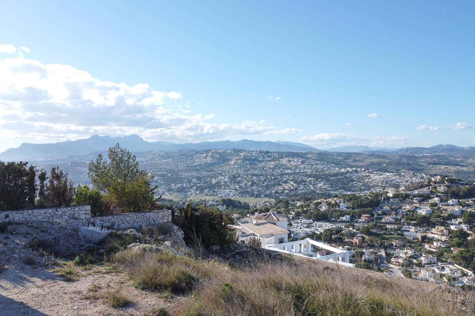 Panoramablick auf Moraira von einem Hügel aus, mit Blick auf das Stadtbild und die fernen Berge.
