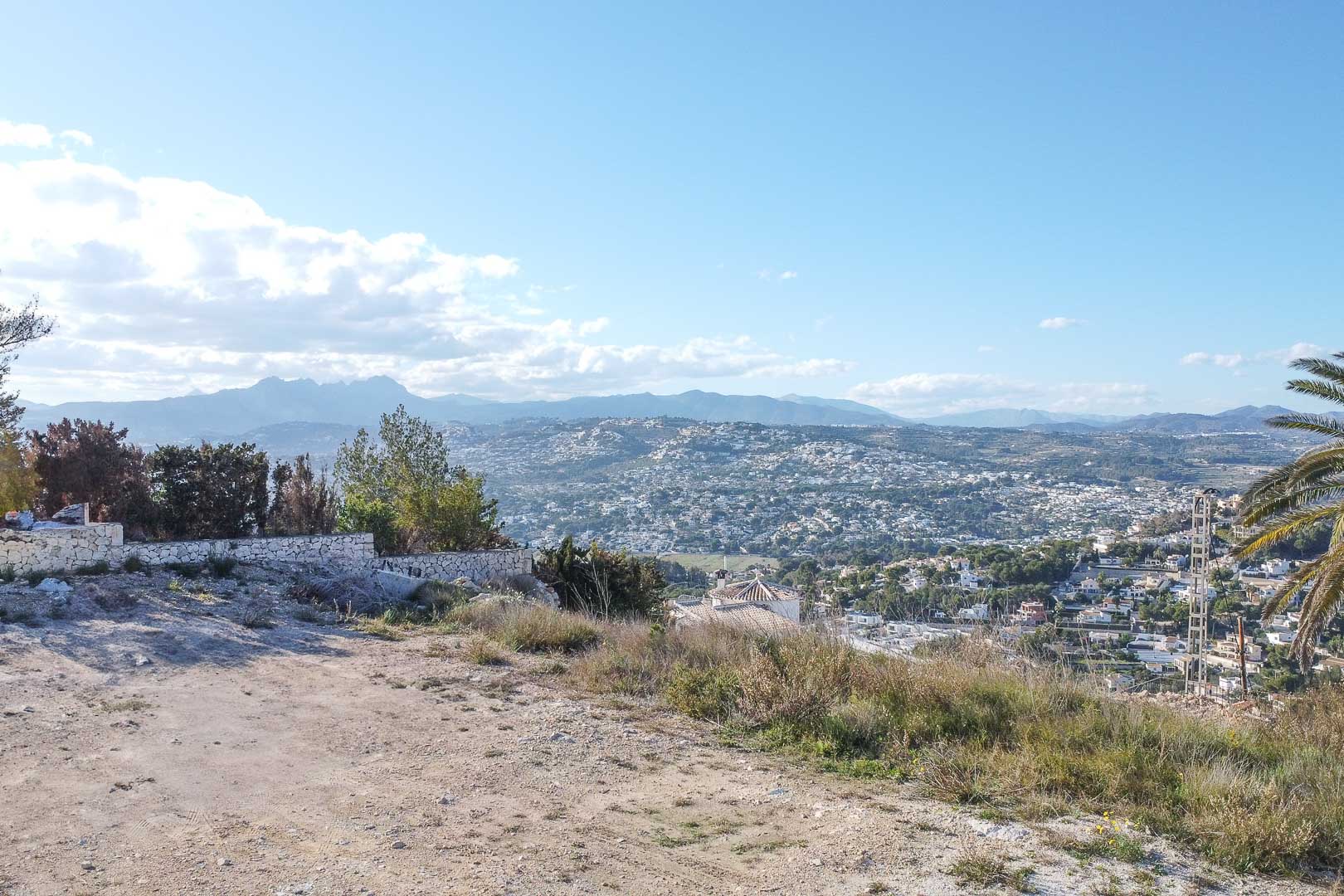 Panoramablick auf Moraira von erhöhtem Grundstück mit Steinmauer und Vegetation.