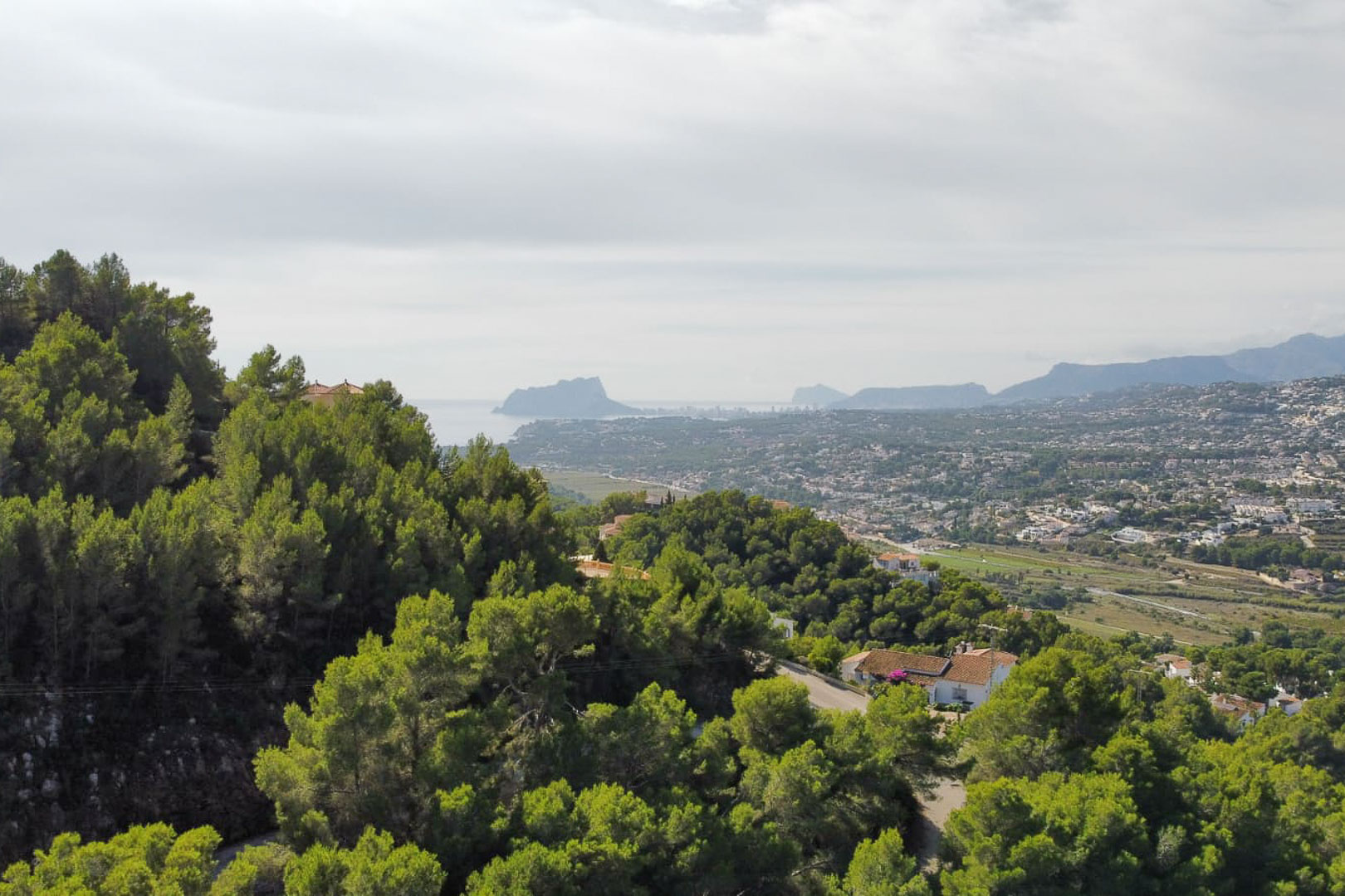 Erhöhter Panoramablick vom Grundstück in Paichi über dichte Pinienwälder und das Wohntal bis hin zur Silhouette des Peñón de Ifach am Meereshorizont.