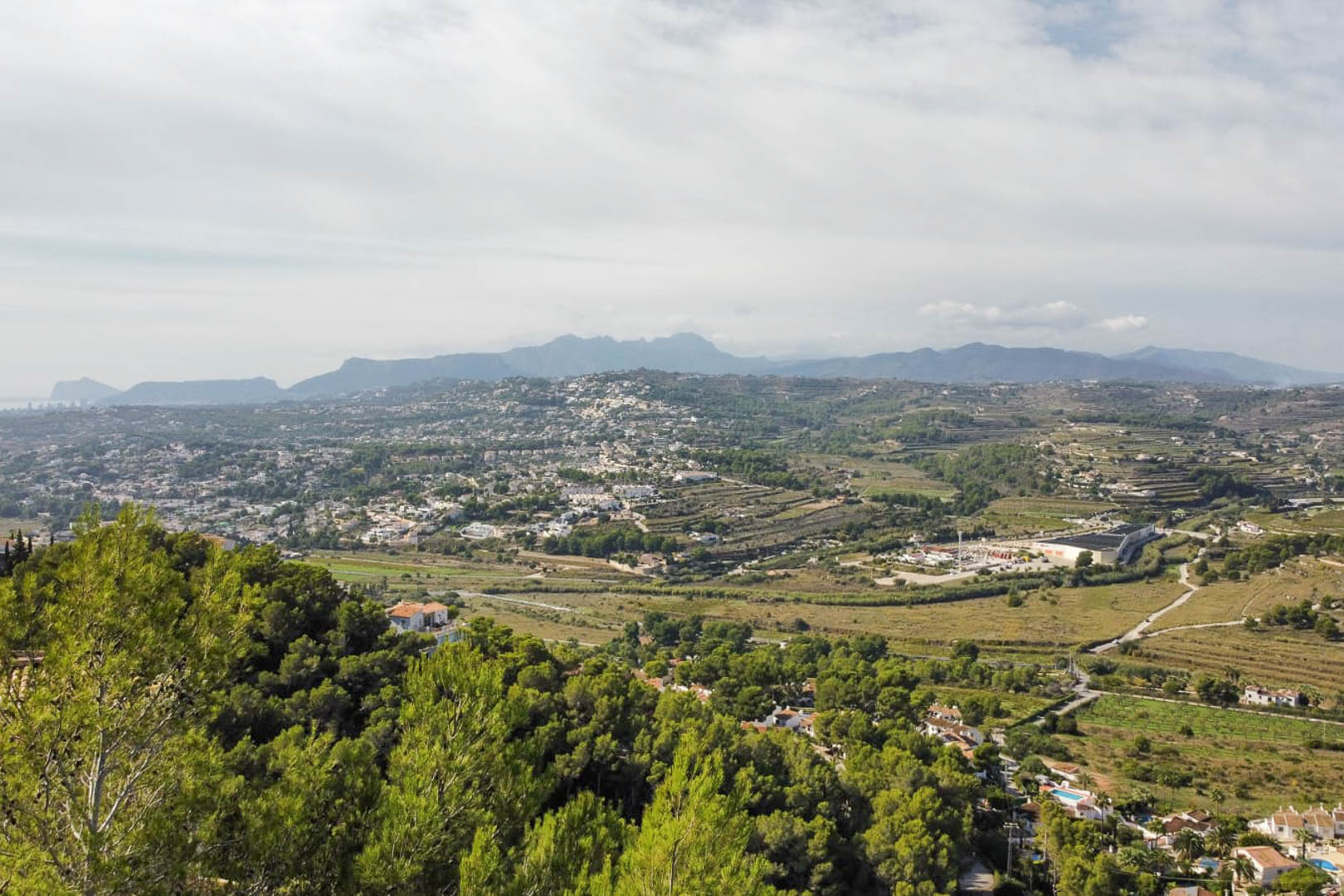 Erhöhter Panoramablick vom Grundstück über das Tal von Moraira, mit dichten Pinienwäldern und fernen Bergketten am Horizont.