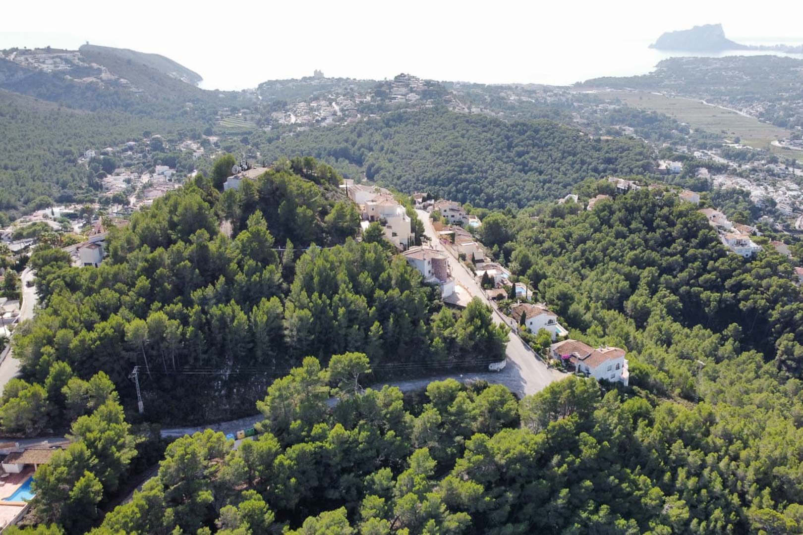 Luftaufnahme des Wohngebiets Paichi in Moraira, die die erhöhte Lage in bewaldeten Hügeln mit Blick auf das Meer und den Peñón de Ifach zeigt.