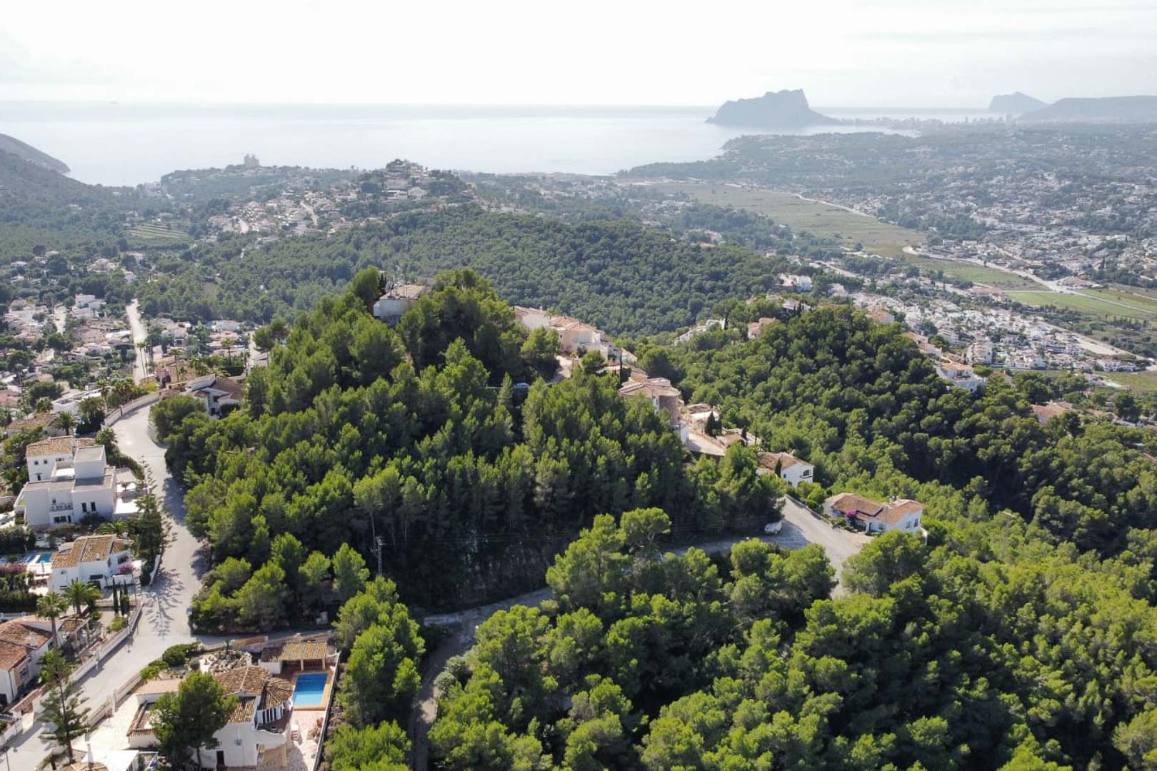 Luftaufnahme des Wohngebiets Paichi in Moraira mit dichtem Pinienwald und Panoramablick auf das Mittelmeer und den Peñón de Ifach in der Ferne.