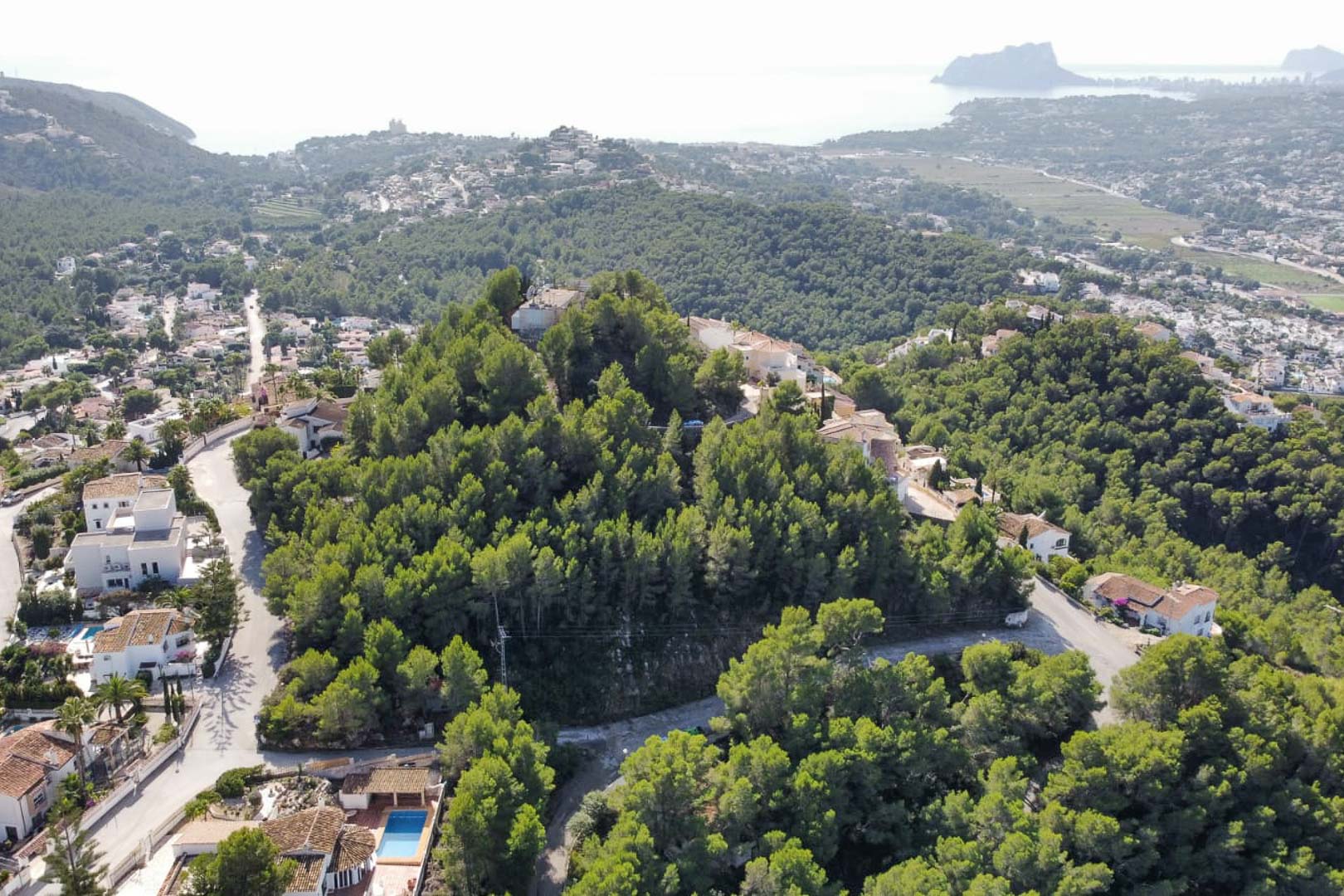Luftbild des bewaldeten Hügels in Paichi, das die erhöhte Lage des Grundstücks mit Blick auf den Peñón de Ifach und das Mittelmeer zeigt.