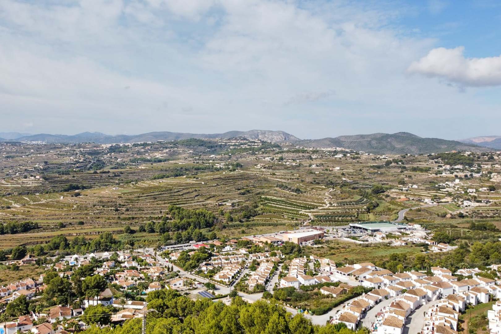 Panorama-Luftaufnahme aus dem Gebiet Paichi mit Blick auf weiße Wohnsiedlungen, terrassierte Hänge und die markante Gebirgskette im Hintergrund.
