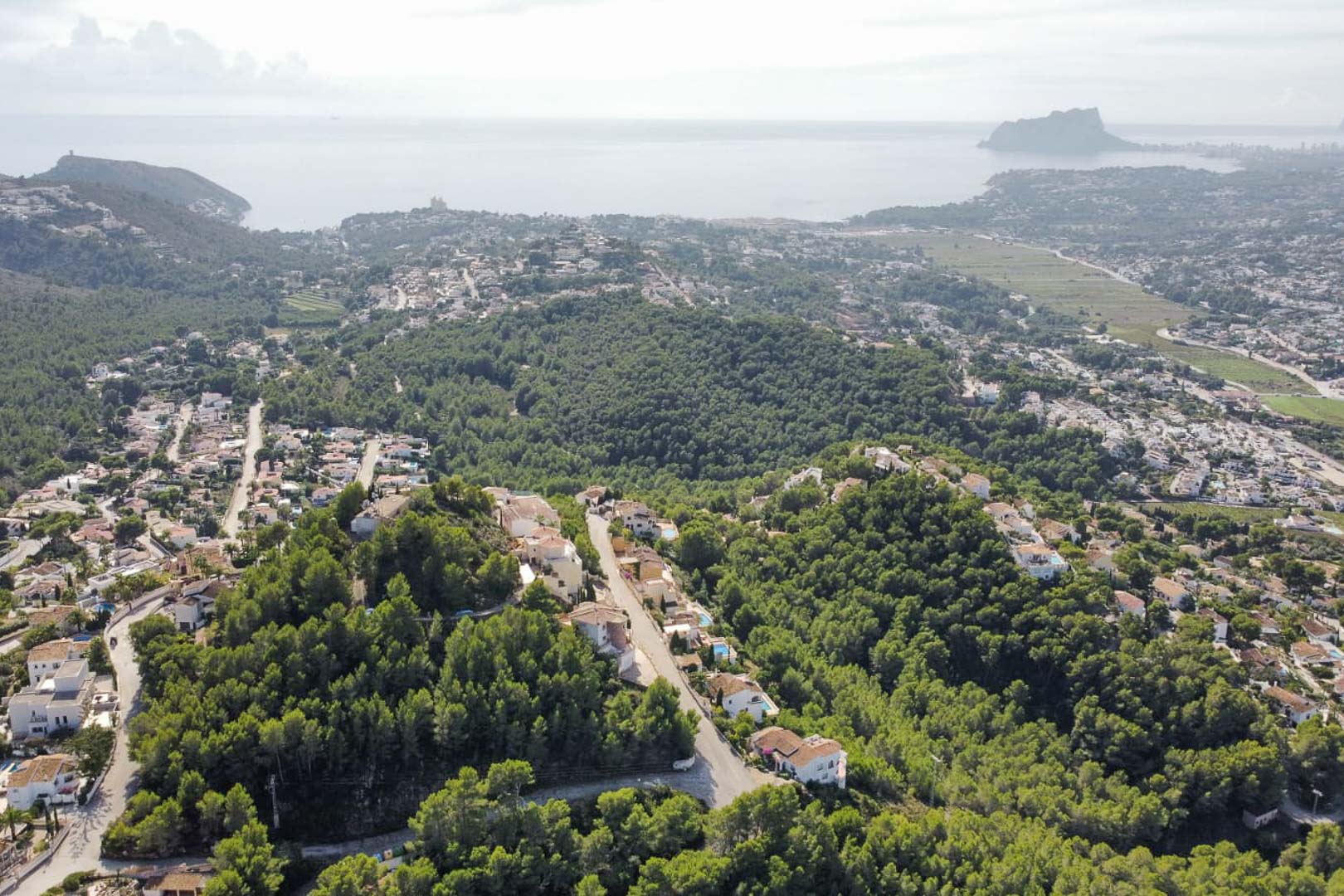 Panorama-Luftaufnahme des Wohngebiets Paichi mit dichten Pinienwäldern, Villen und dem markanten Peñón de Ifach am Horizont des Mittelmeers.