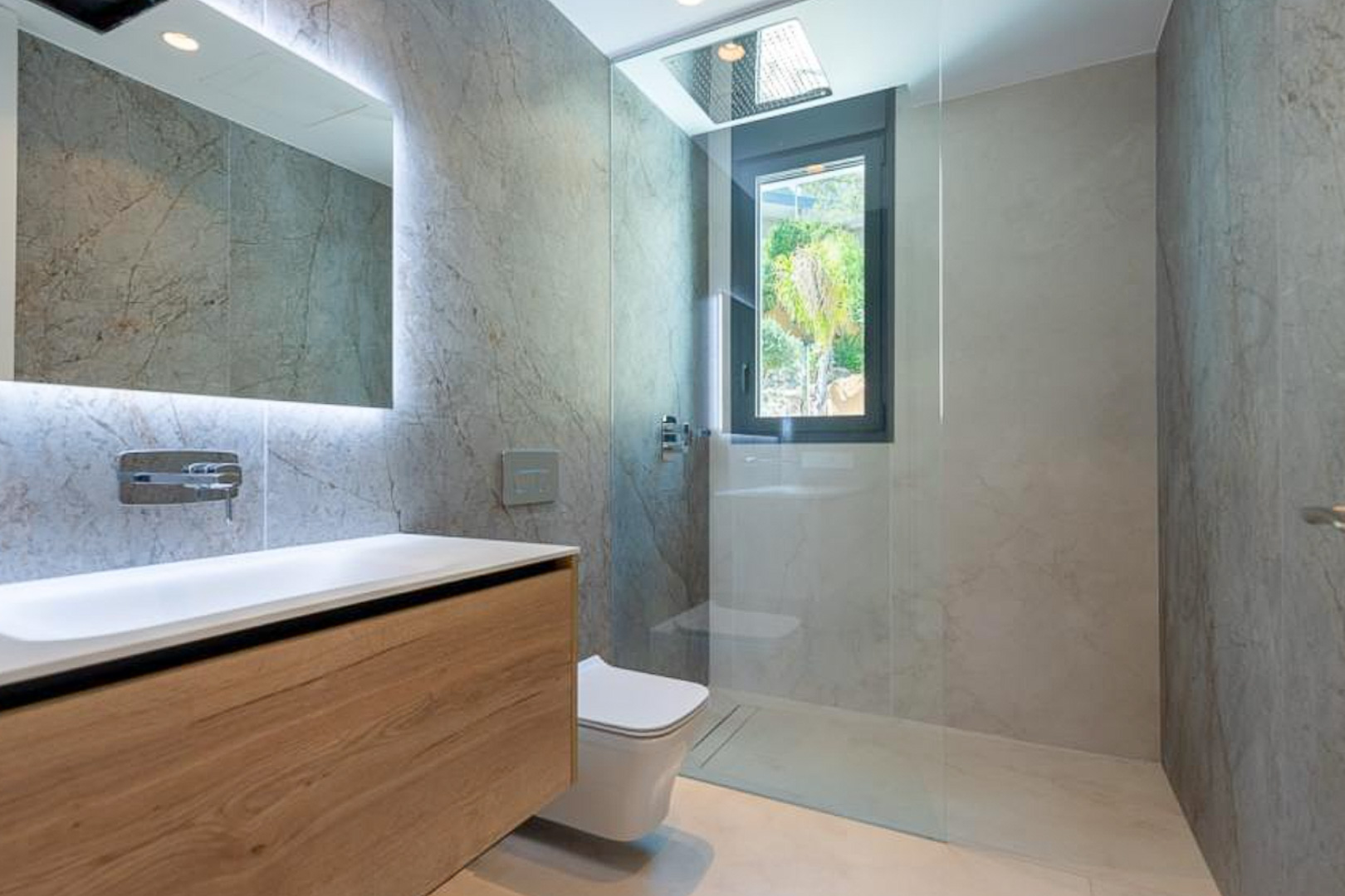 Design-Badezimmer mit Wandfliesen in Steinoptik, schwebendem Holzwaschtisch, hinterleuchtetem Spiegel und ebenerdiger Dusche mit Deckenbrause.
