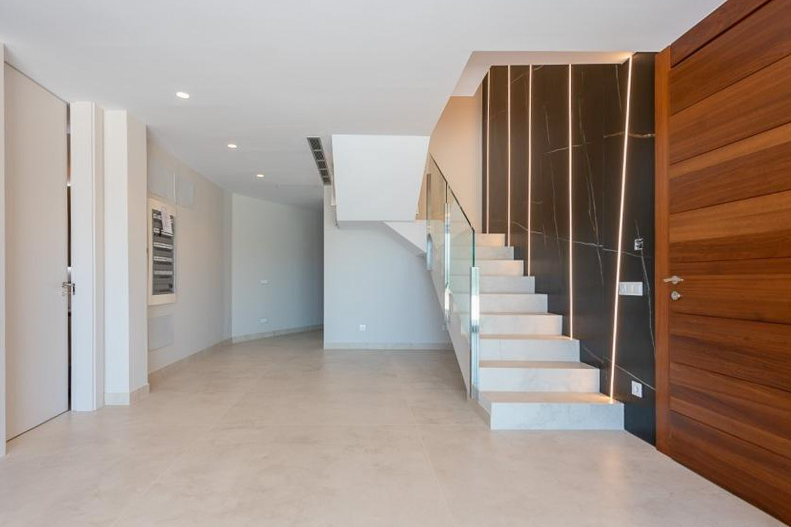 Eingangsbereich mit weißer Steintreppe, Glasgeländer und einer dunklen Akzentwand in Marmoroptik mit vertikalen LED-Lichtleisten.