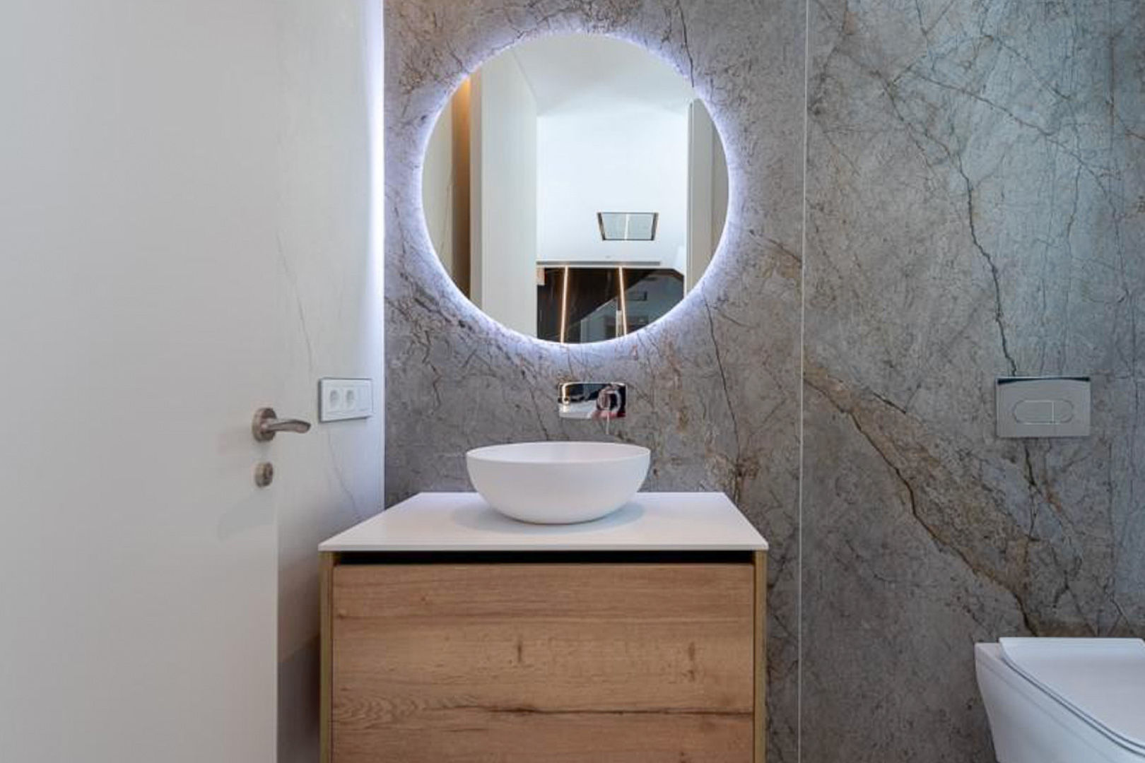 Gäste-WC mit grauen Marmoreffekt-Fliesen, hinterleuchtetem Rundspiegel und Holz-Waschtisch mit Aufsatzbecken sowie Unterputz-Armatur.