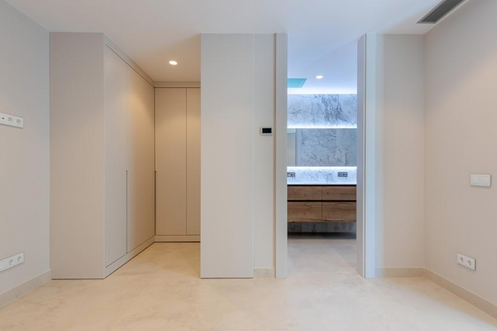 Hauptschlafzimmer mit raumhohen Einbauschränken und En-Suite-Bad, ausgestattet mit Marmorwänden, einem Holzwaschtisch und integrierter LED-Beleuchtung.