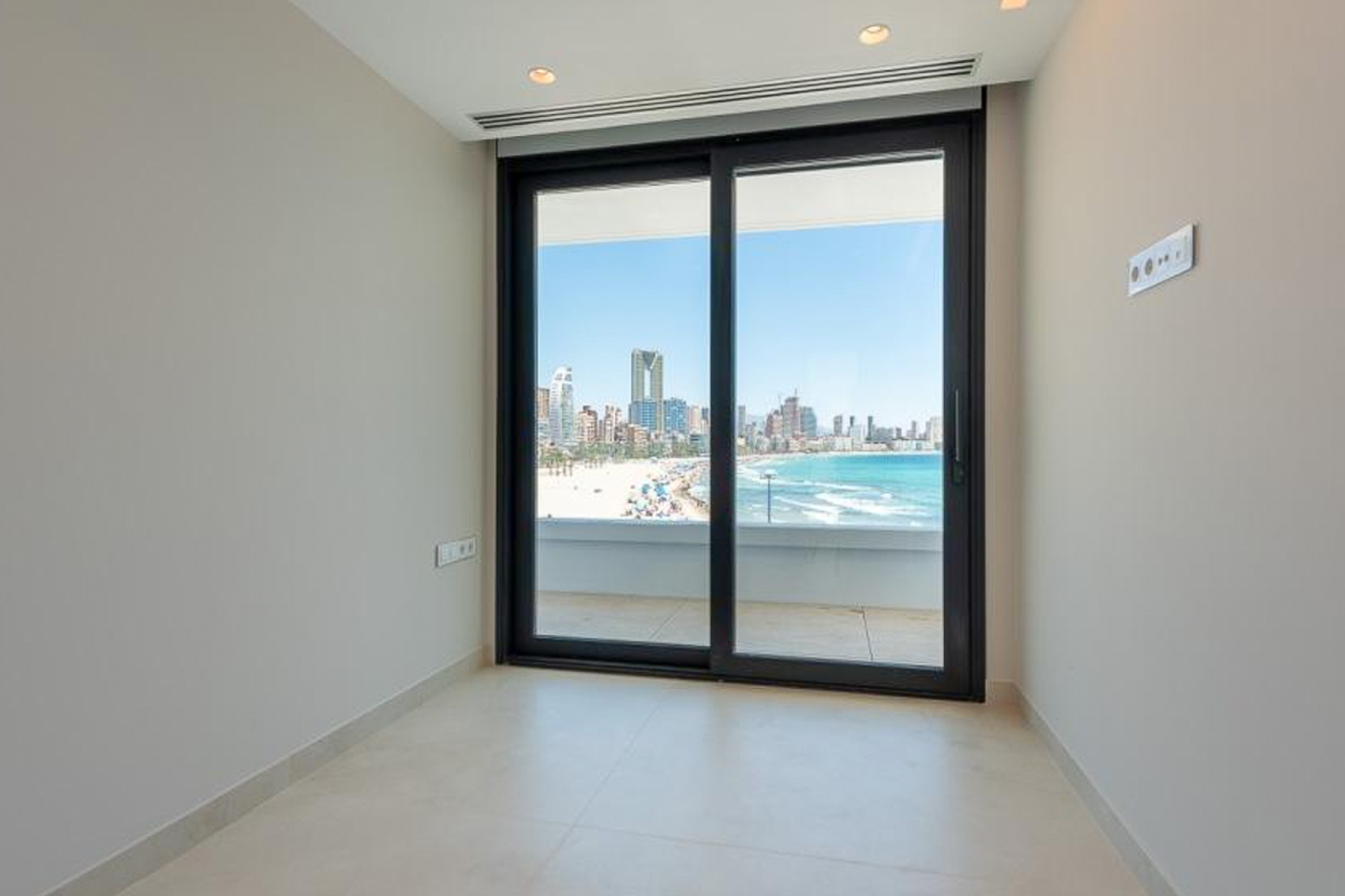 Heller Innenraum mit hellem Feinsteinzeug und bodentiefen Glasschiebetüren mit Panoramablick auf den Strand und die Skyline von Benidorm.
