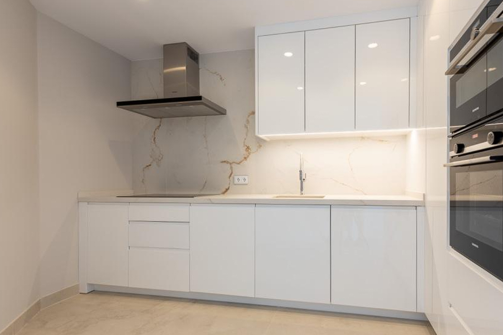 Minimalistische Designerküche mit grifflosen weißen Schränken, einer Rückwand in Marmoroptik und hochwertigen integrierten Einbaugeräten.