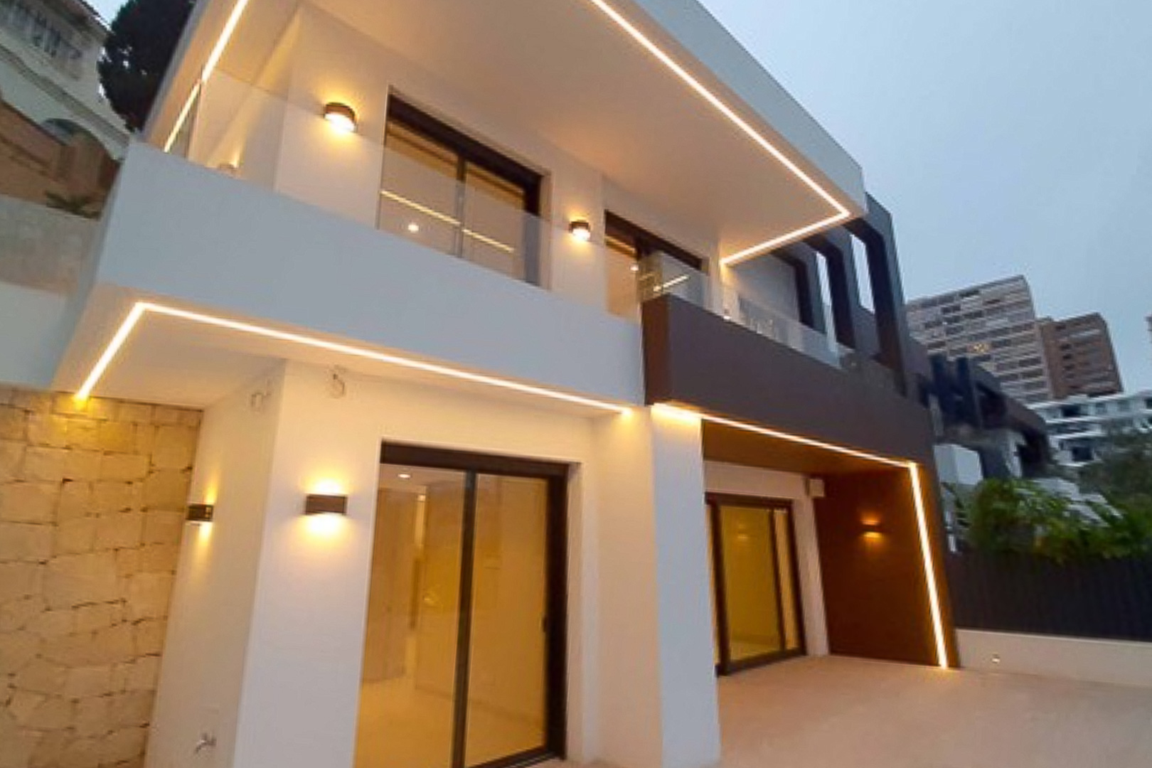 Moderne Außenfassade mit integrierter LED-Beleuchtung, Glasgeländern und großen Glasschiebetüren in minimalistischem Design.
