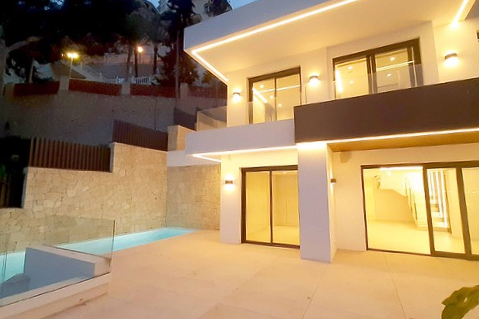 Moderne Fassade mit integrierter LED-Beleuchtung, Feinsteinzeug-Terrasse und privatem Pool vor Natursteinwänden.