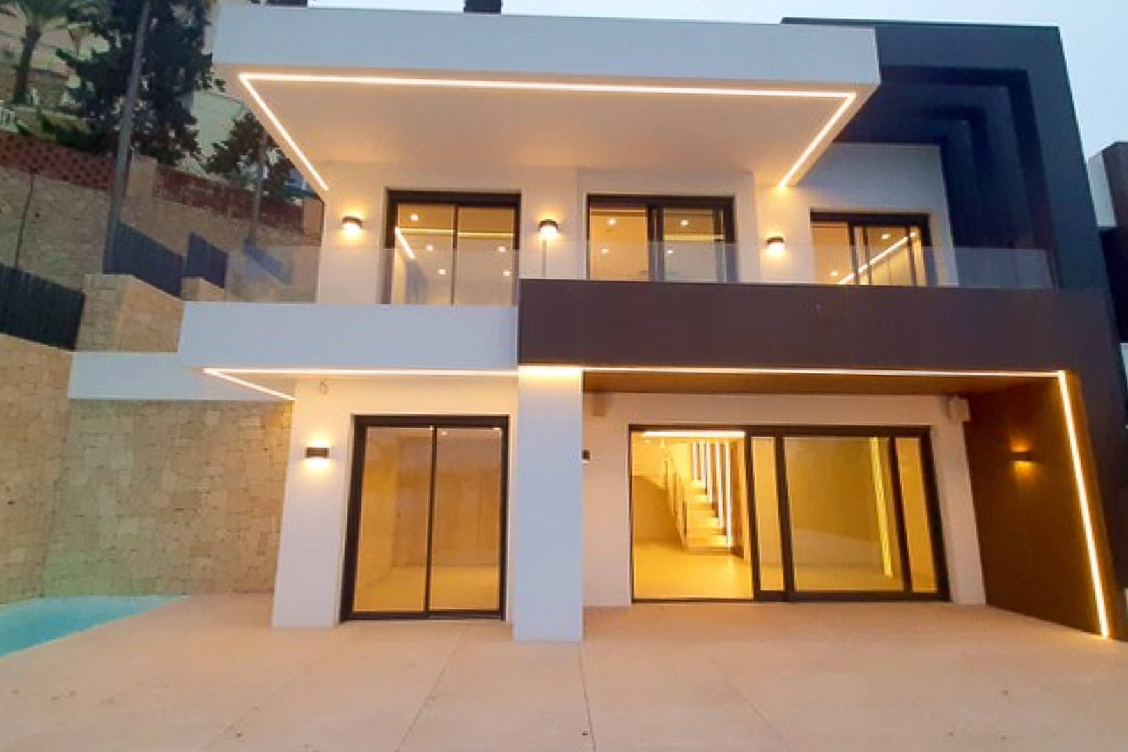 Moderne Fassade mit integrierter LED-Beleuchtung, großen Glasschiebetüren und Terrassen mit Glasgeländern im Kontrast zwischen weißen und dunklen Bauelementen.