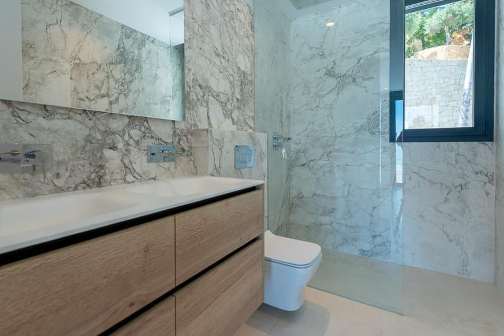 Modernes Badezimmer mit Wandverkleidung in Marmoroptik, Doppelwaschtisch aus hellem Holz und begehbarer Dusche mit Glastrennwand.